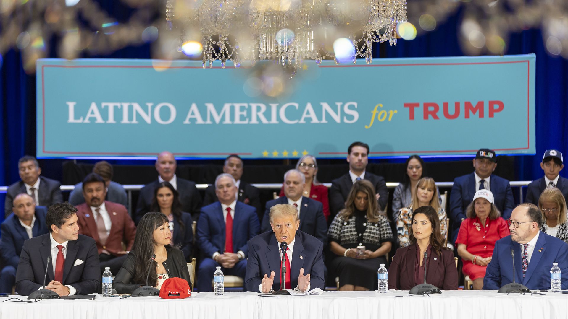 President Donald Trump surrounded by people with a "Latino Americans for Trump" banner hanging in the background.