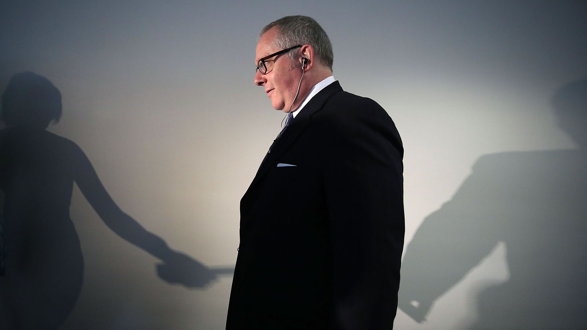 Caputo walks down a hallway while wearing a suit jacket