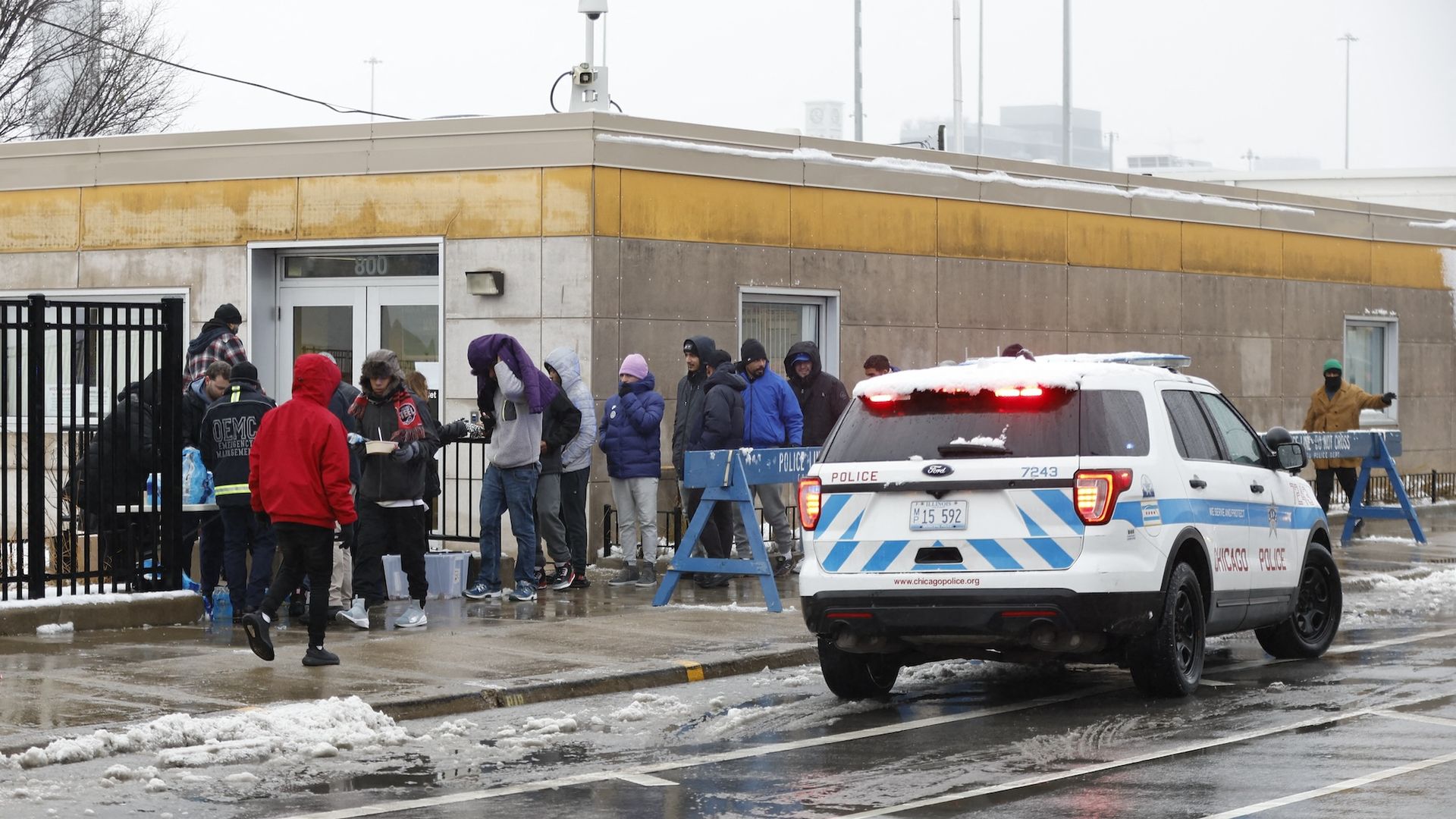 Migrants outside, wearing winter clothes with a Chicago police car.