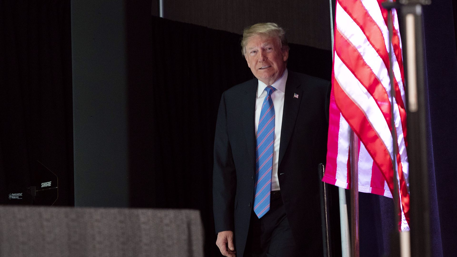 Donald Trump walking on stage peering from behind an American Flag