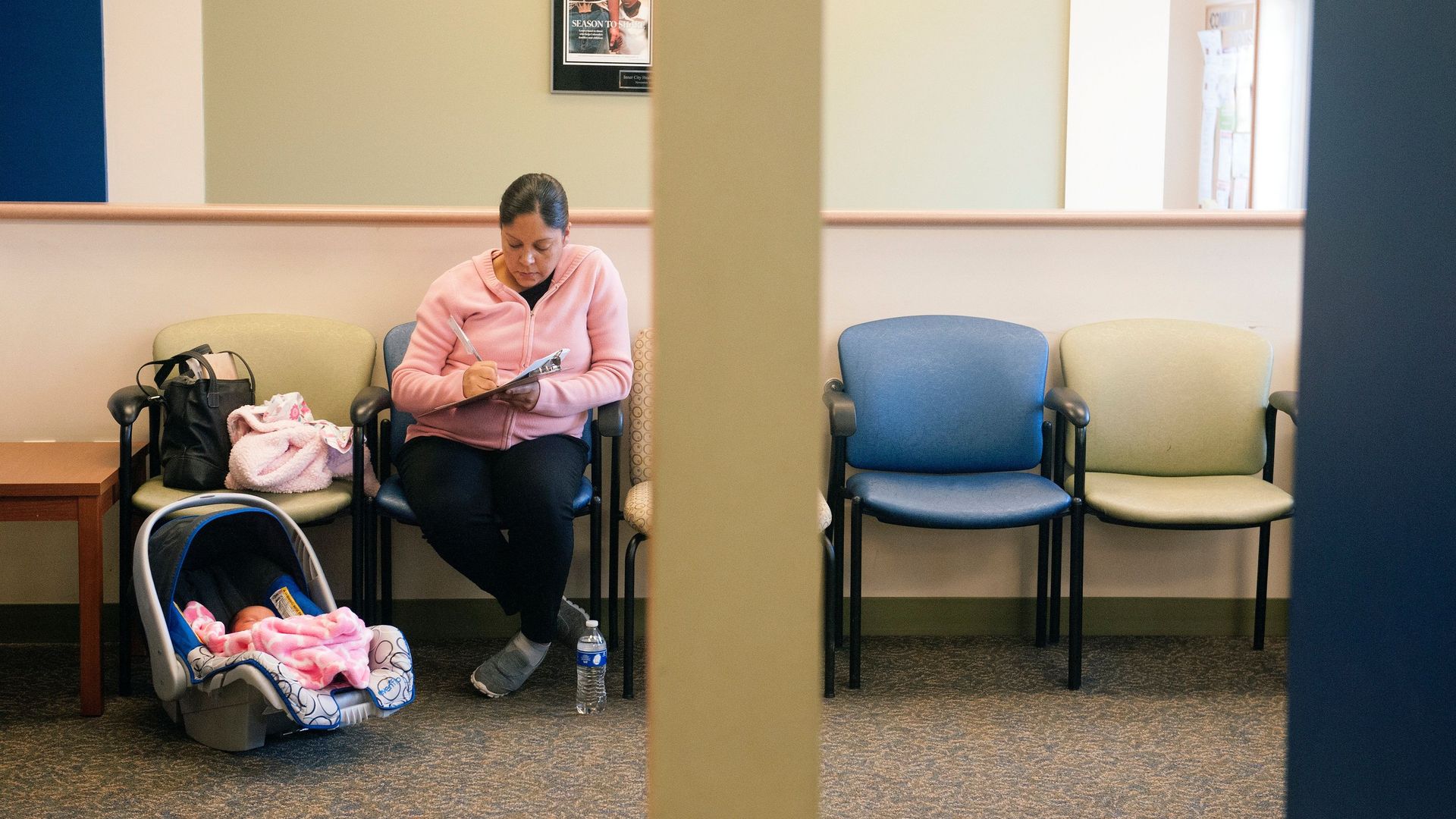 A woman sits in a doctor's office with her infant filling out paperwork.