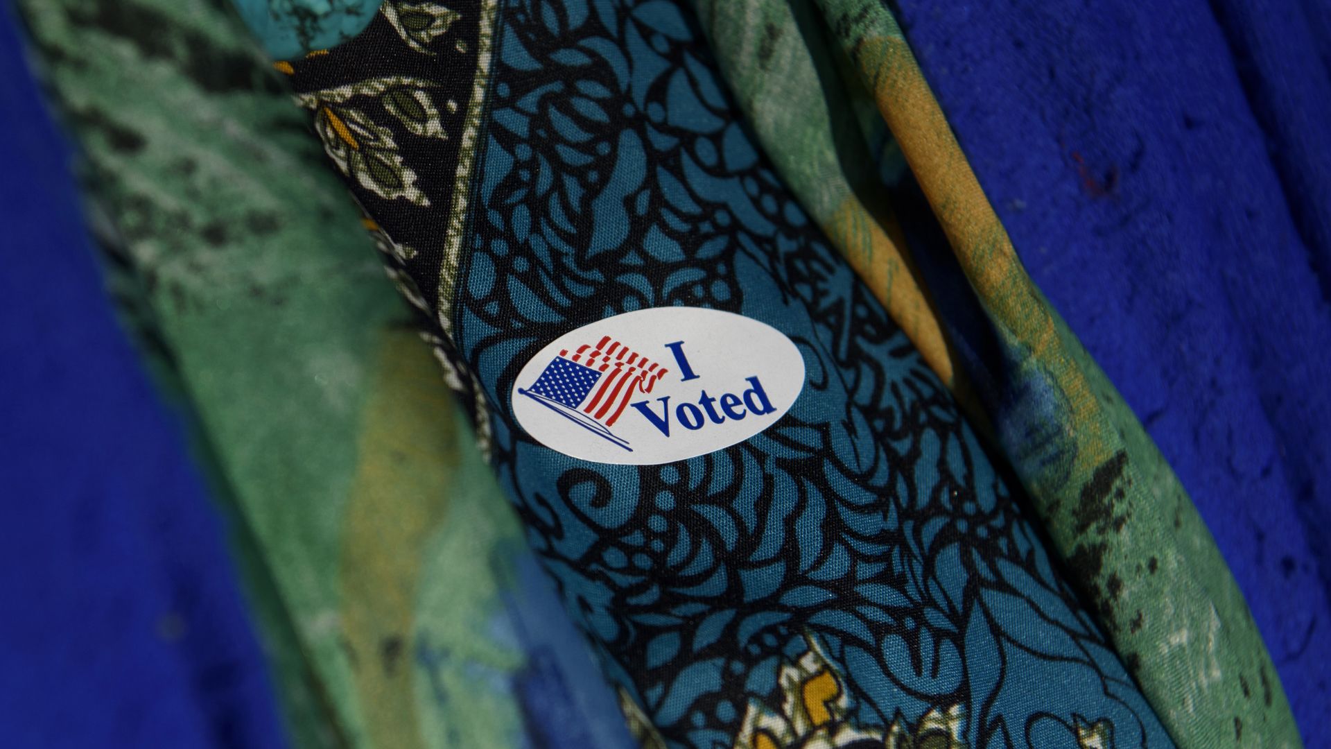 A voter dons an "I Voted" sticker on her blue and green top with gold lace
