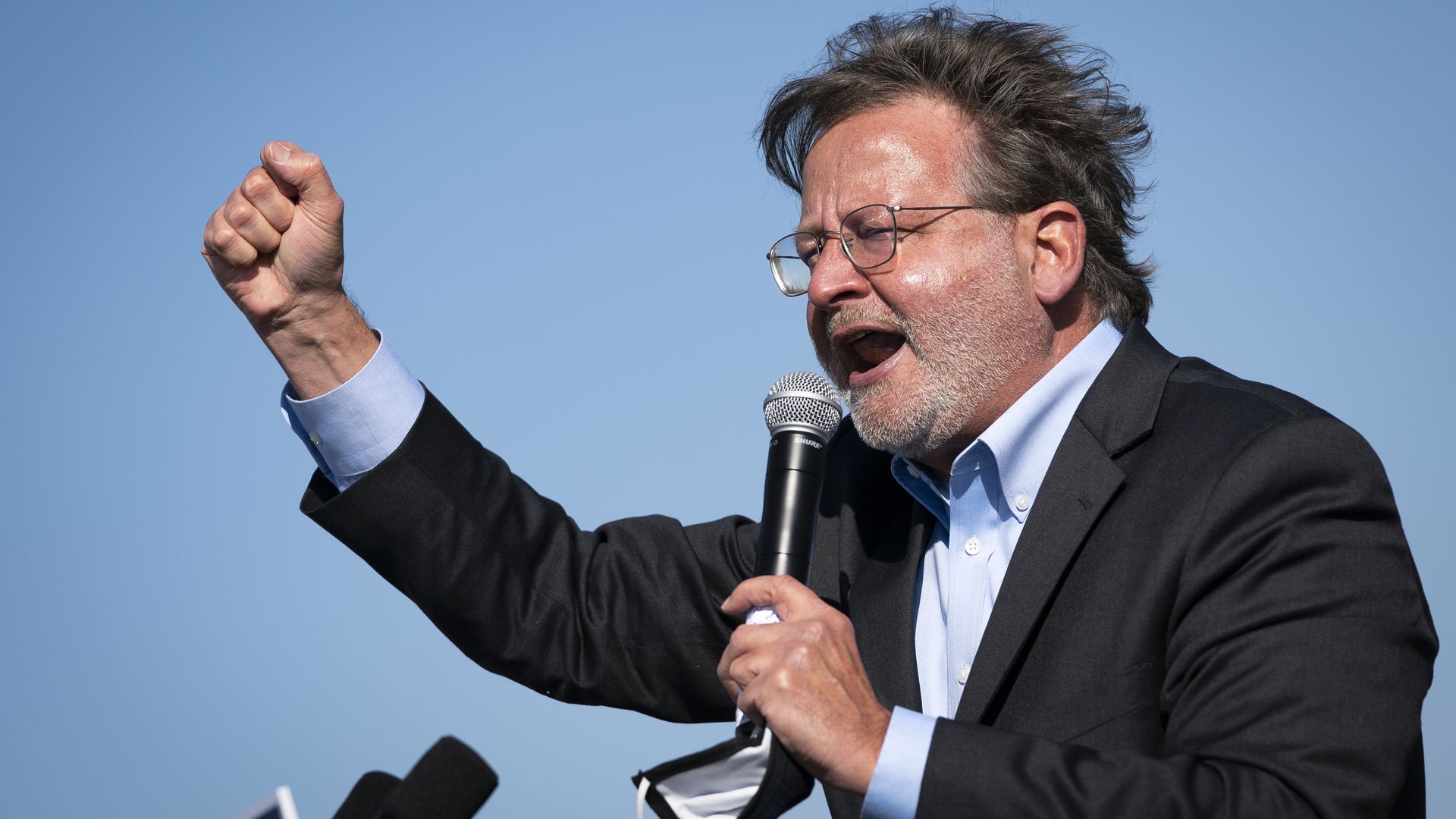 Gary Peters holds a face mask and a microphone