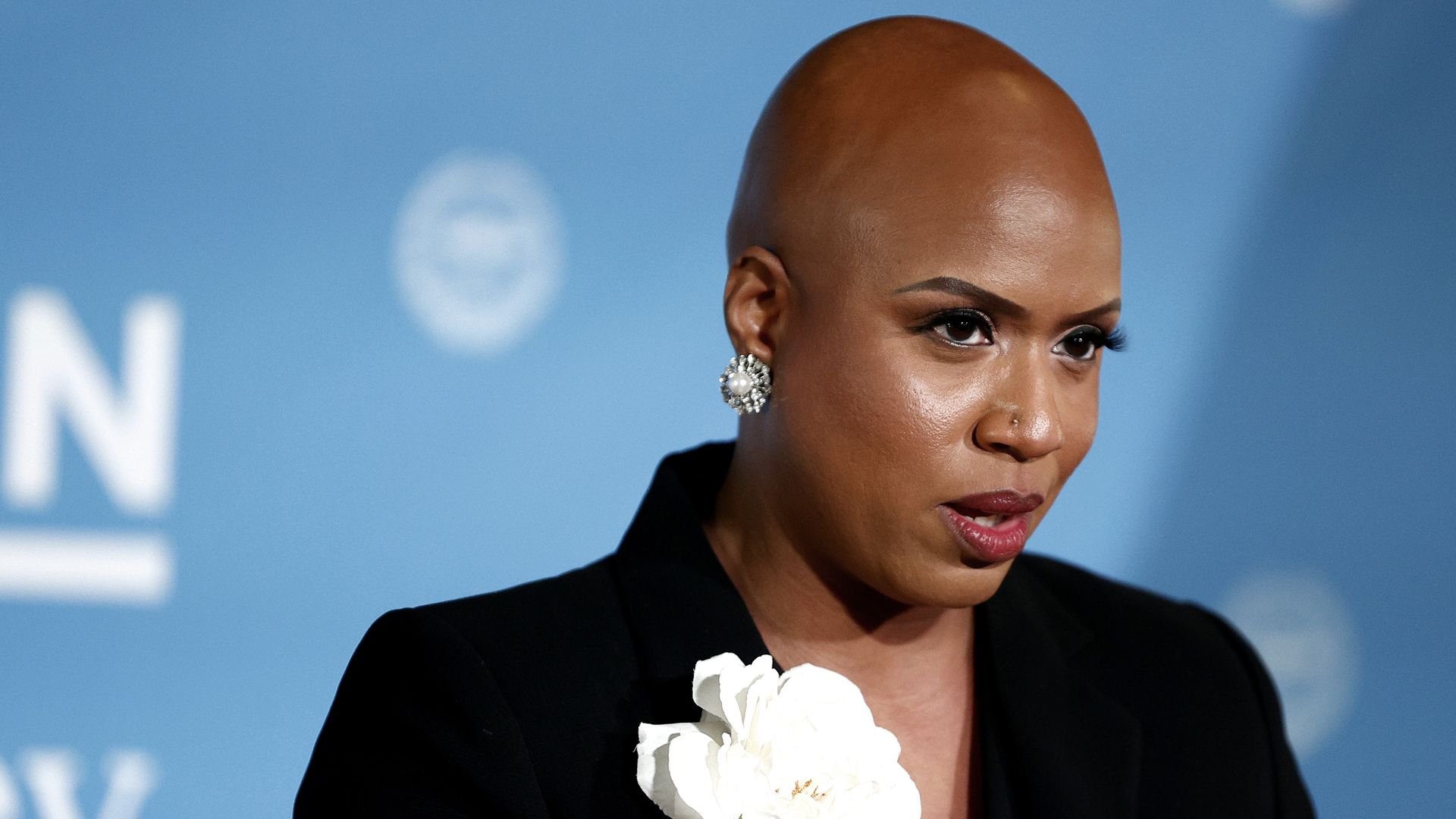 Photo of Ayanna Pressley wearing a black suit that has a white flower on it as she speaks