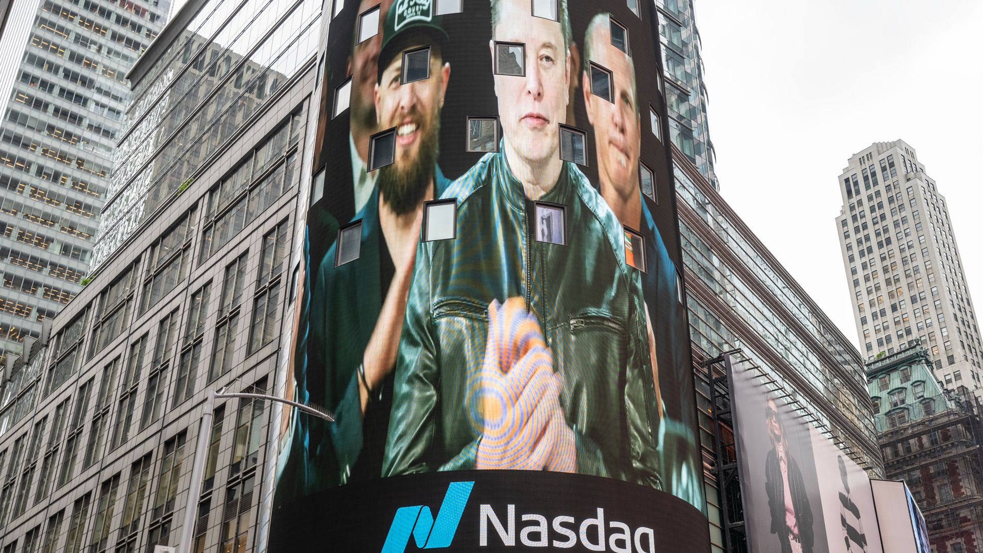 A cylindrical building wrapped in a giant LED screen shows close-up portraits of several men, with the Nasdaq logo at the base and glass skyscrapers surrounding the city.