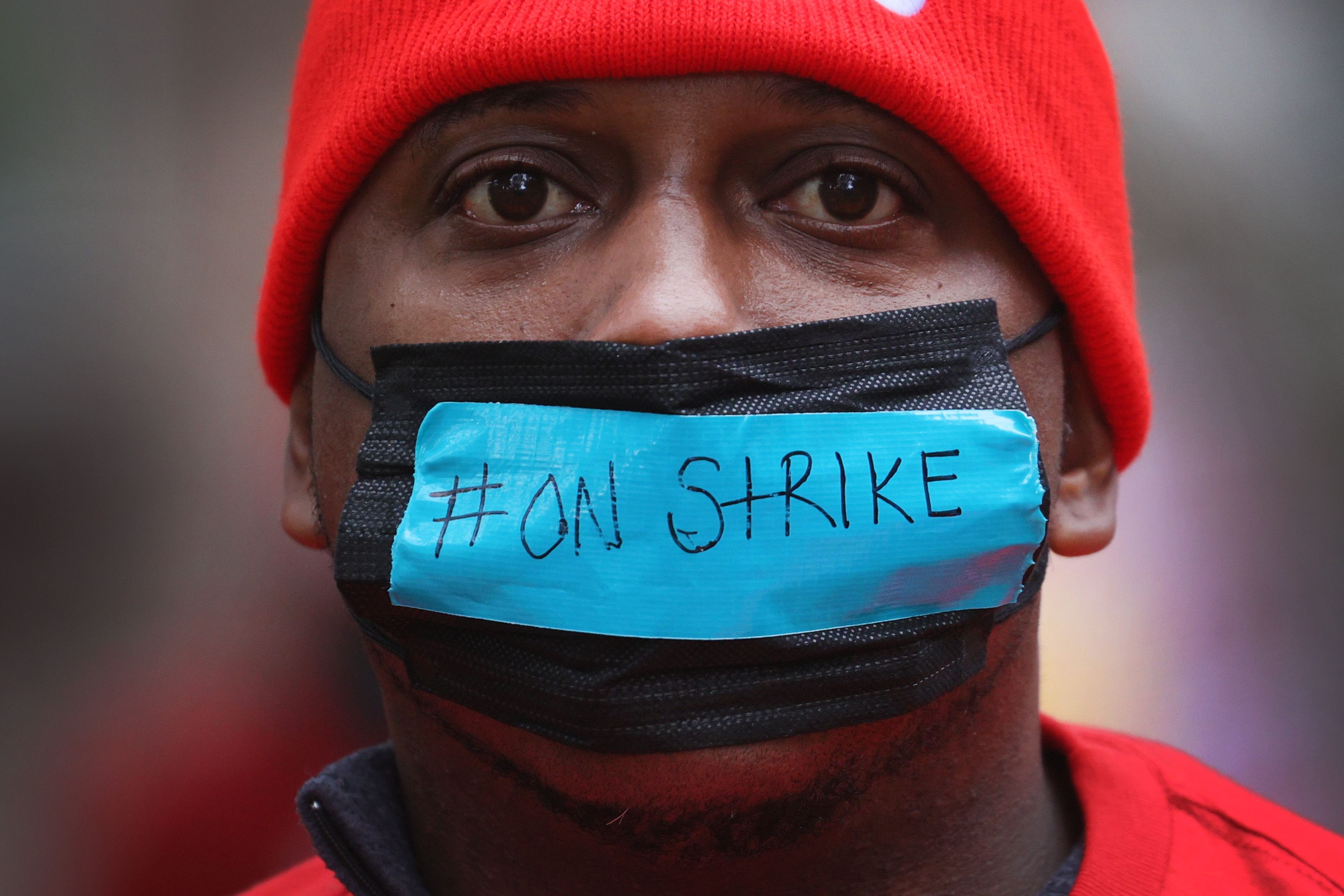 A person wears a face mask that reads: “#On Strike”.