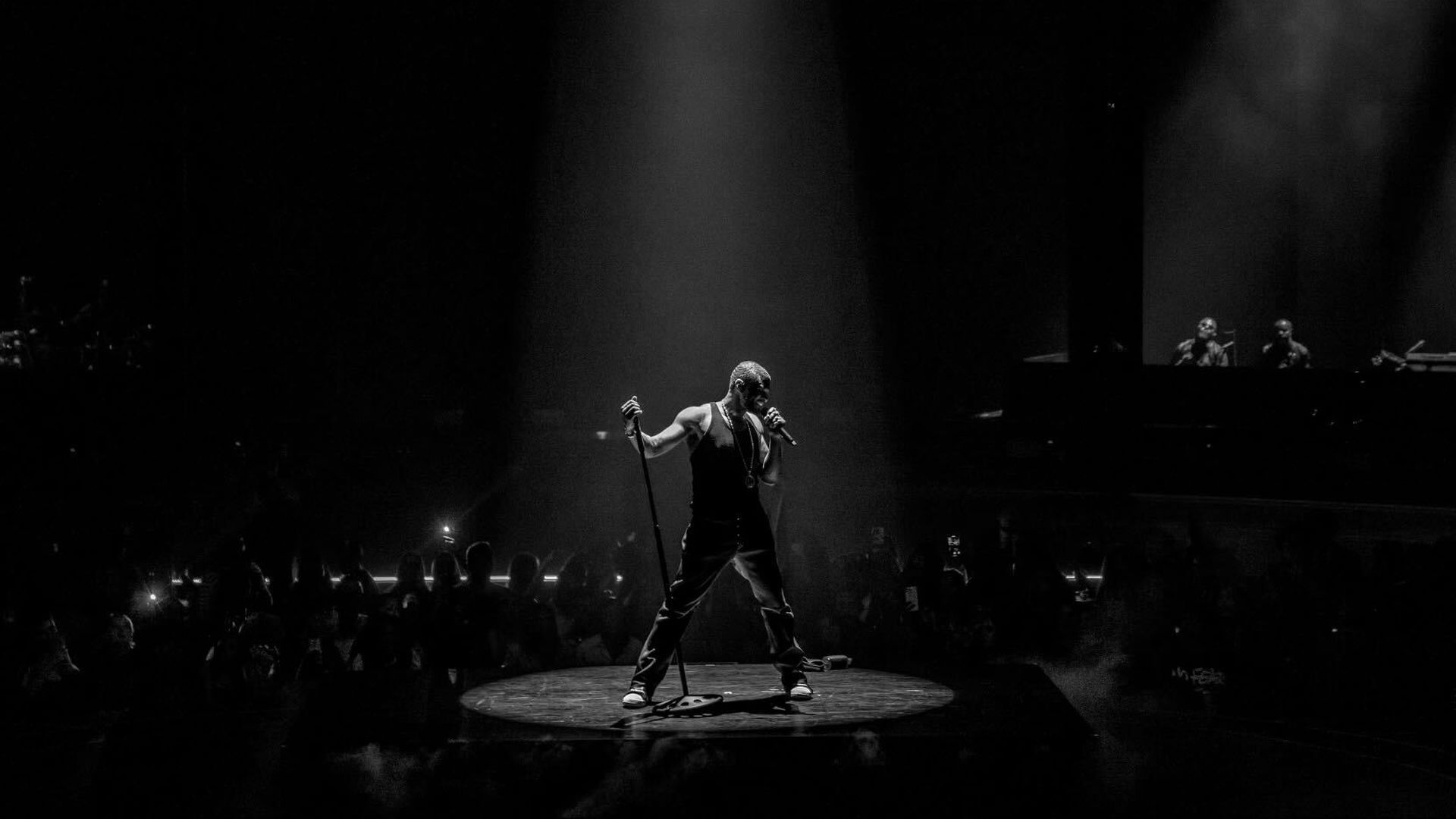 Photo of artist Usher on a stage singing into a microphone. 