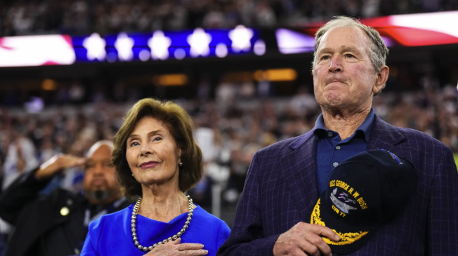 Laura Bush and George W. Bush have their hands on their chests during an anthem at a game