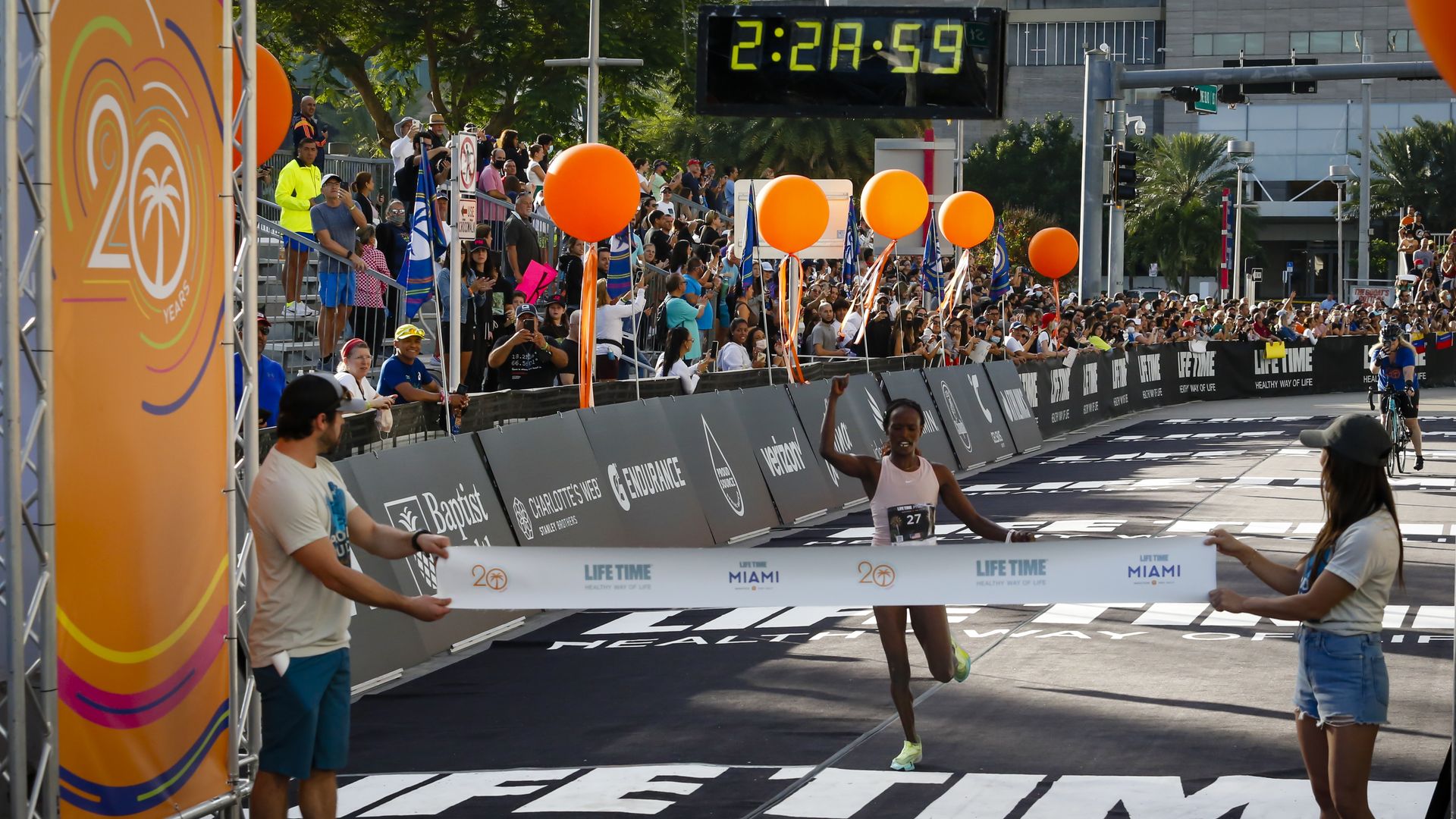 a woman raises her fist triumphantly as she is about to go through a banner to win a marathon 