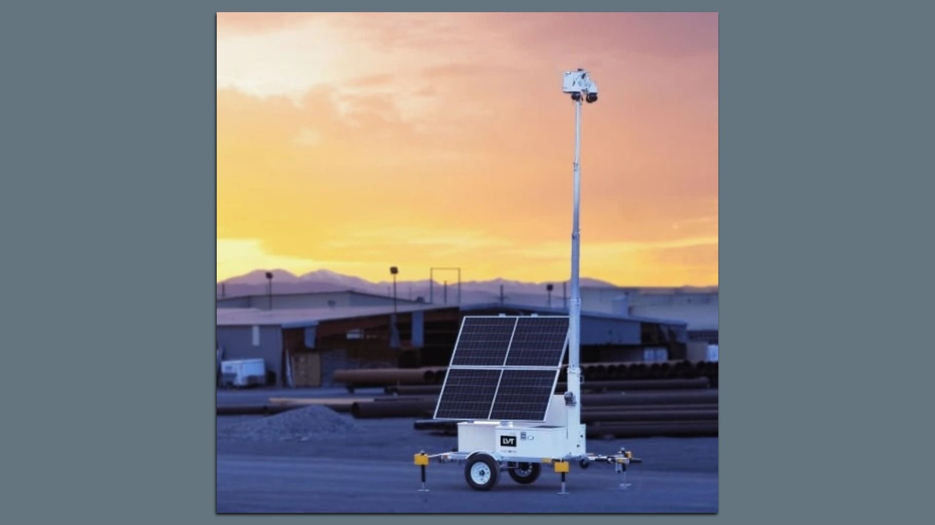 Mobile solar-powered camera tower on a trailer with solar panels, overlooking an industrial yard at sunset.