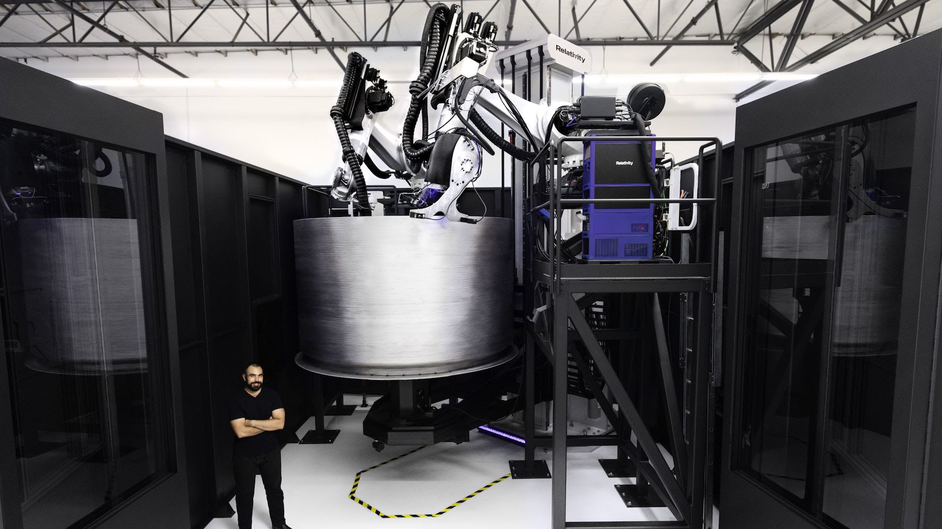 A man stands in front of a metal space device around twice his size. 