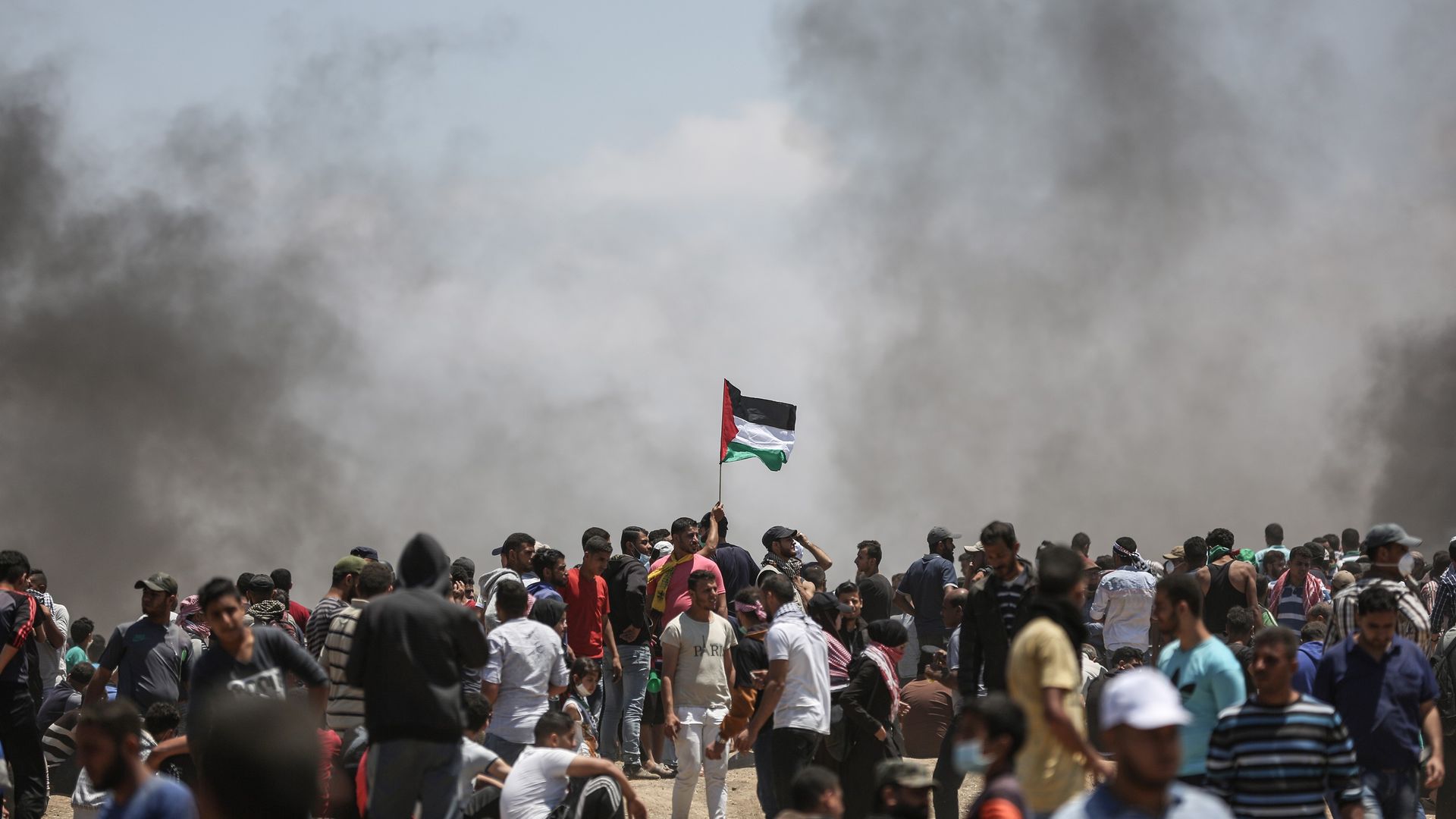 protesters along Gaza border with smoke in background