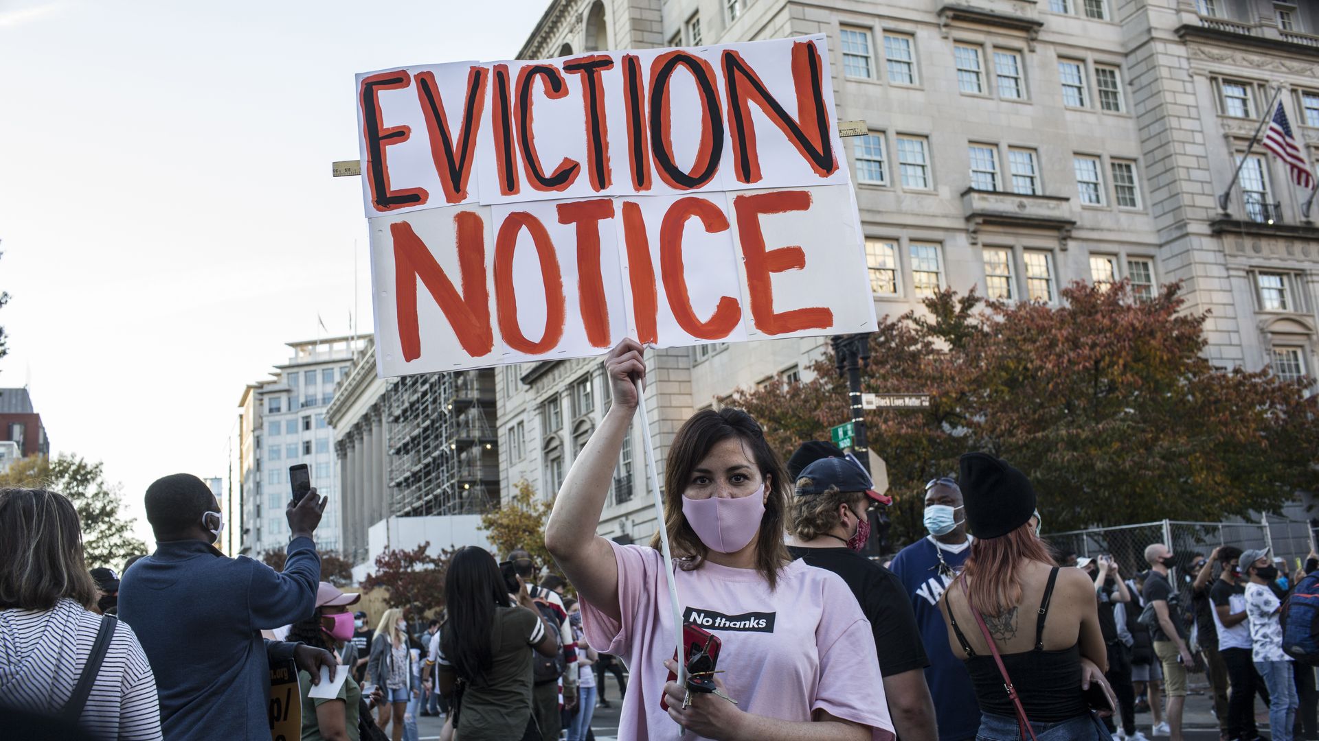Picture of a woman holding a sign that says "Eviction Notice" in the middle of the street, surrounded by Black Lives Matter protesters 