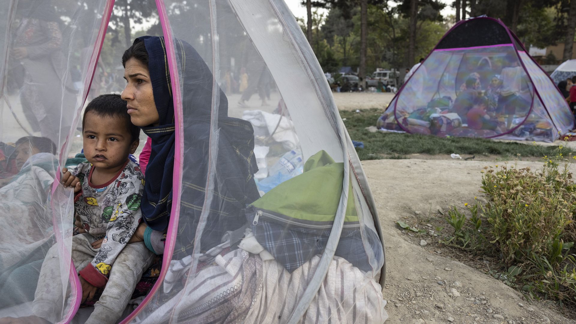 Photo of a woman holding a child in a translucent tent outdoors, looking pensive