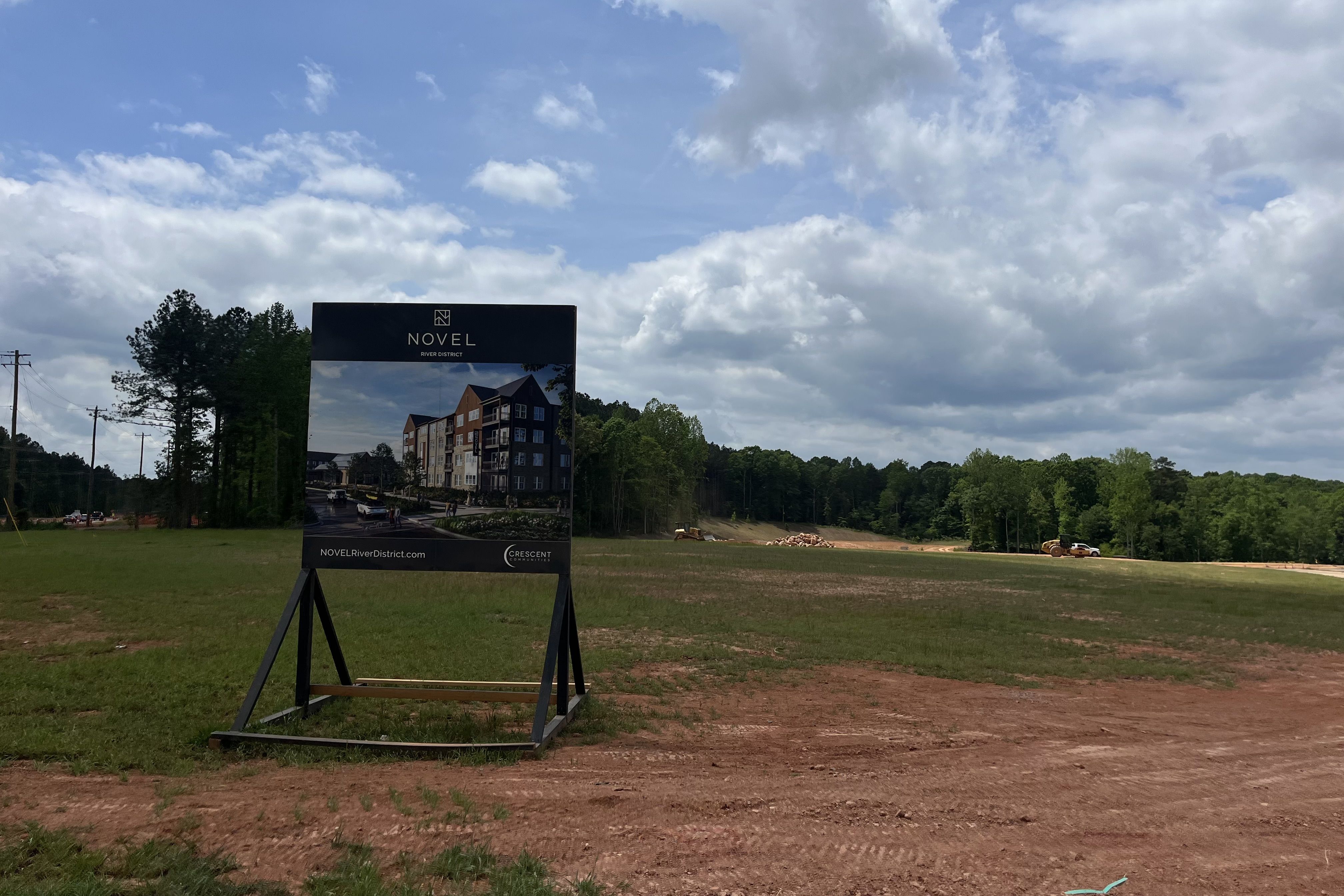 A sign advertising an apartment in front of a big grass lot