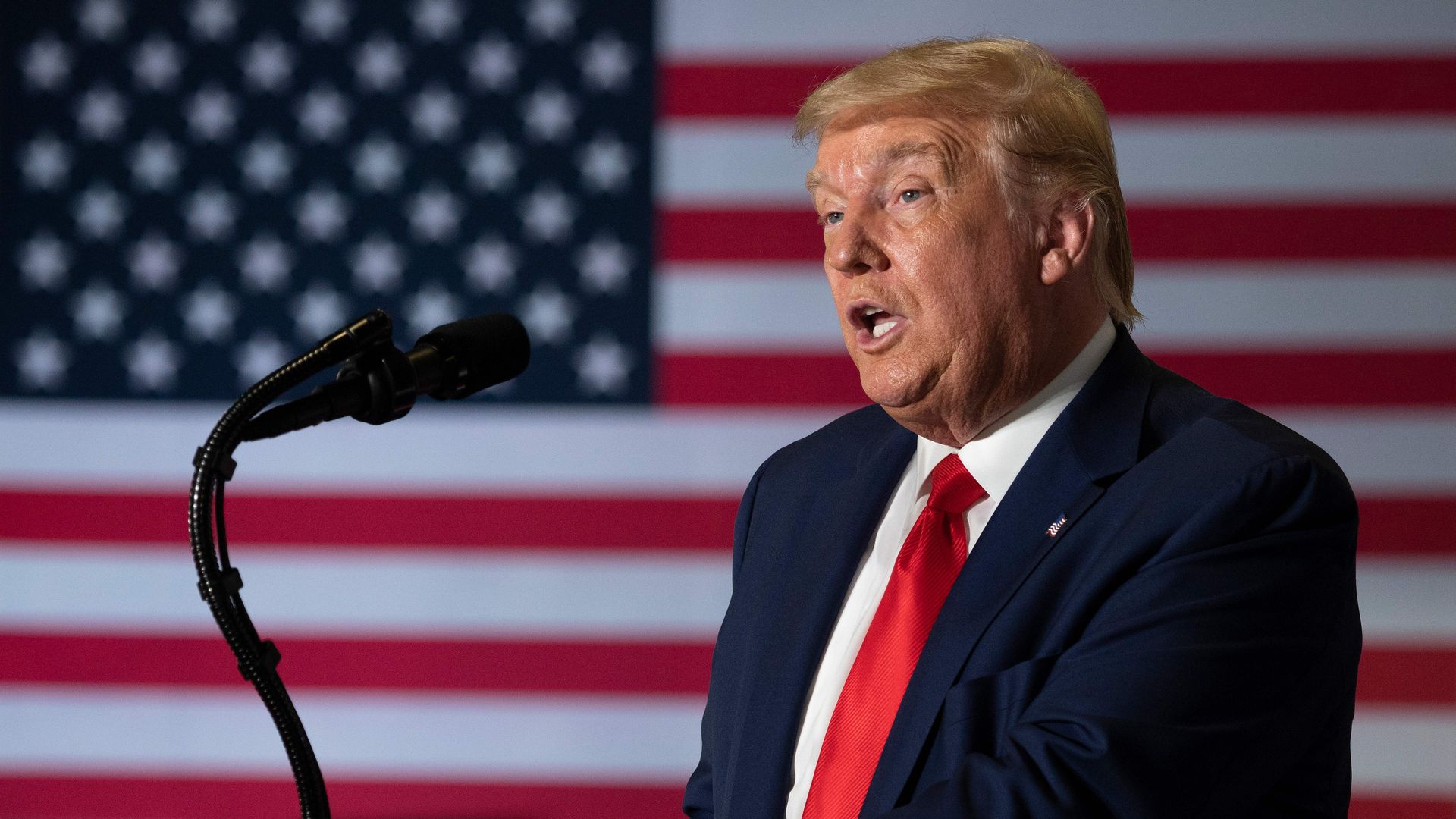 President Trump speaking into a microphone with the US flag in the background