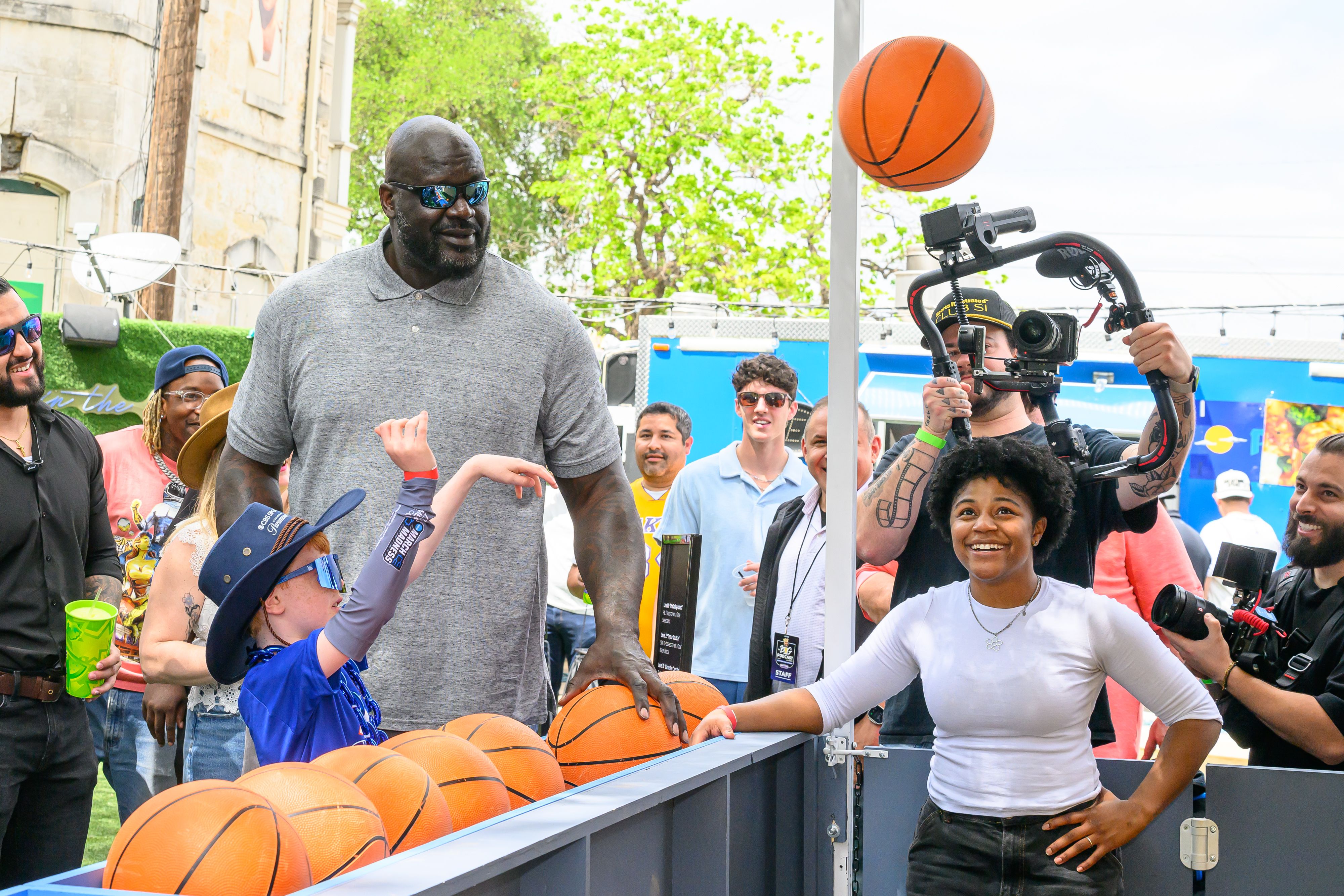 Shaquille O'Neal attends the Shaquille O'Neal Big Pod Event at Home Room San Antonio with a kid throwing a basketball.