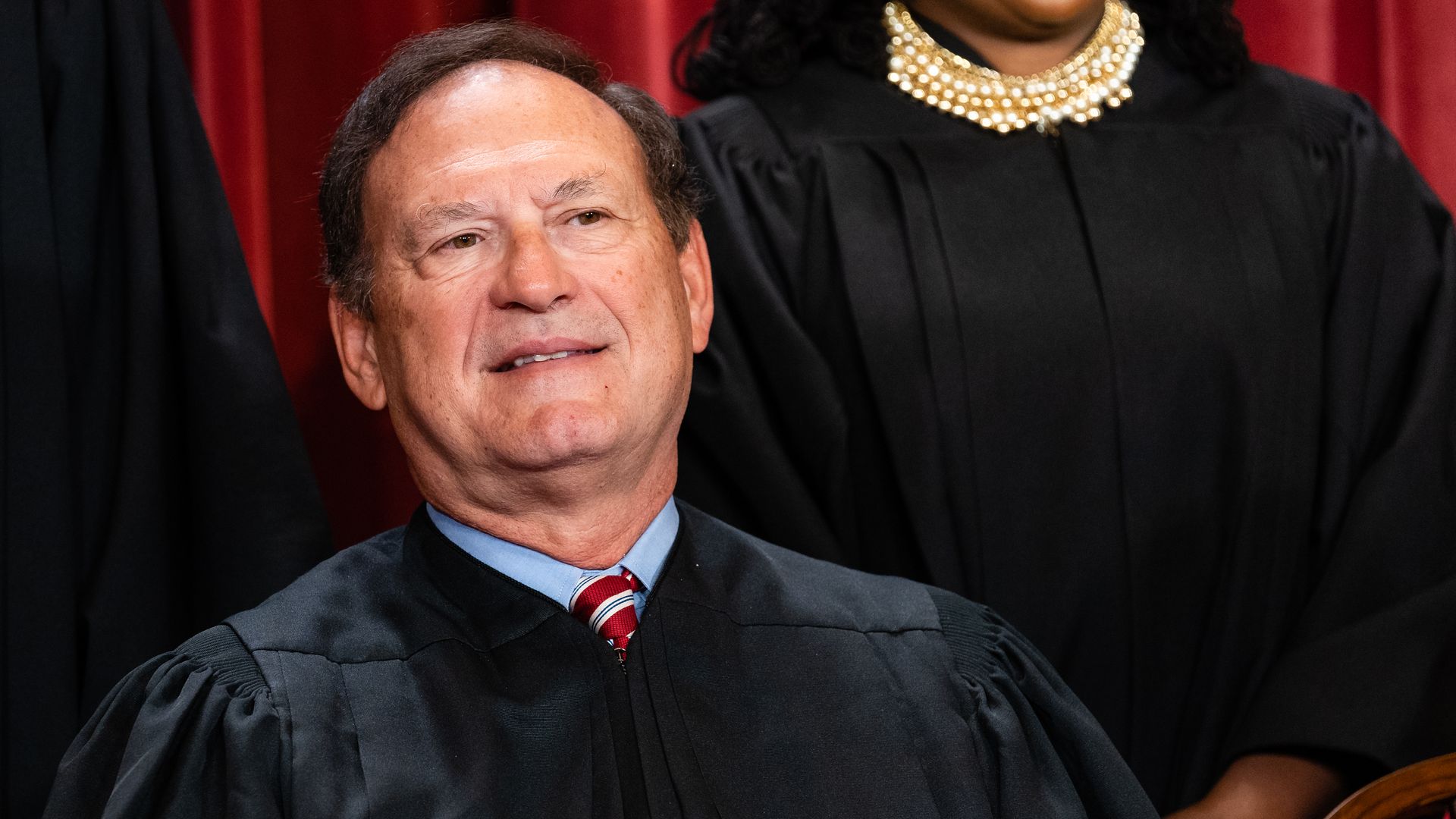 Justice Samuel Alito, wearing black robes, a blue shirt and red tie, surrounded by colleagues.