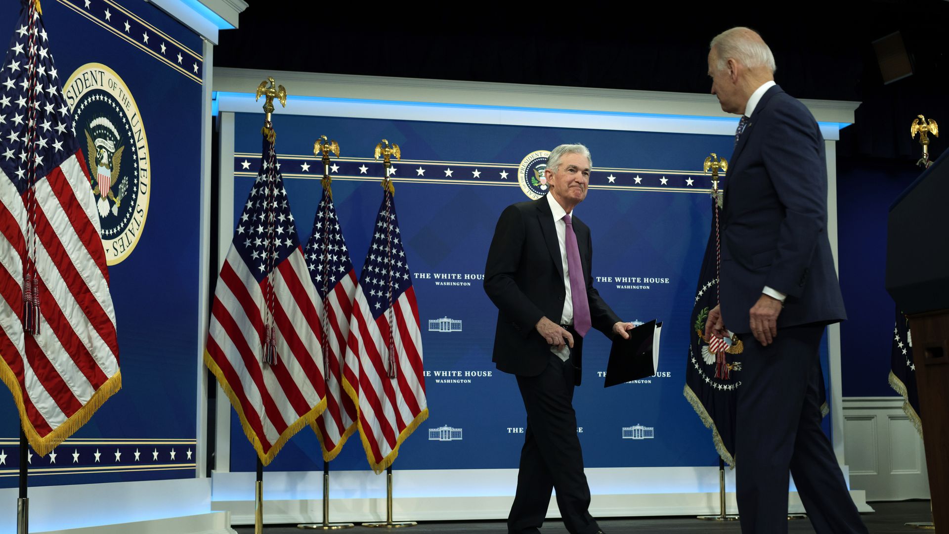 Fed chair Jerome Powell walks to a podium with American flags in the background as President Biden watches