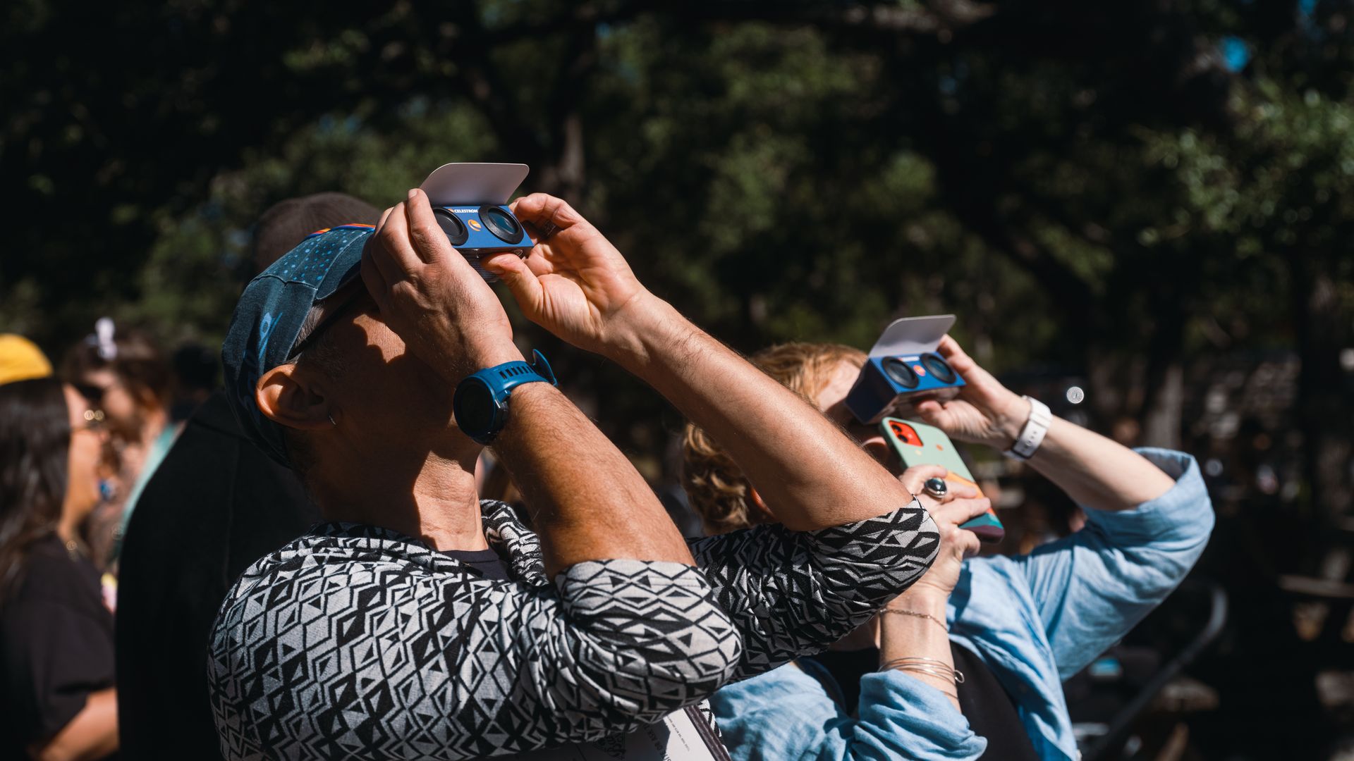 A photo of two people holding glasses up to their face with trees in the background.