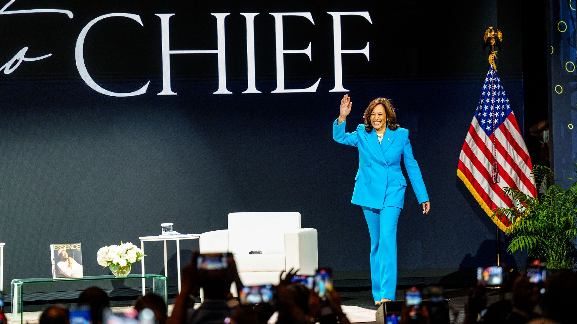 Kamala Harris walks onstage underneath a title that says "Chief" next to an American flag.