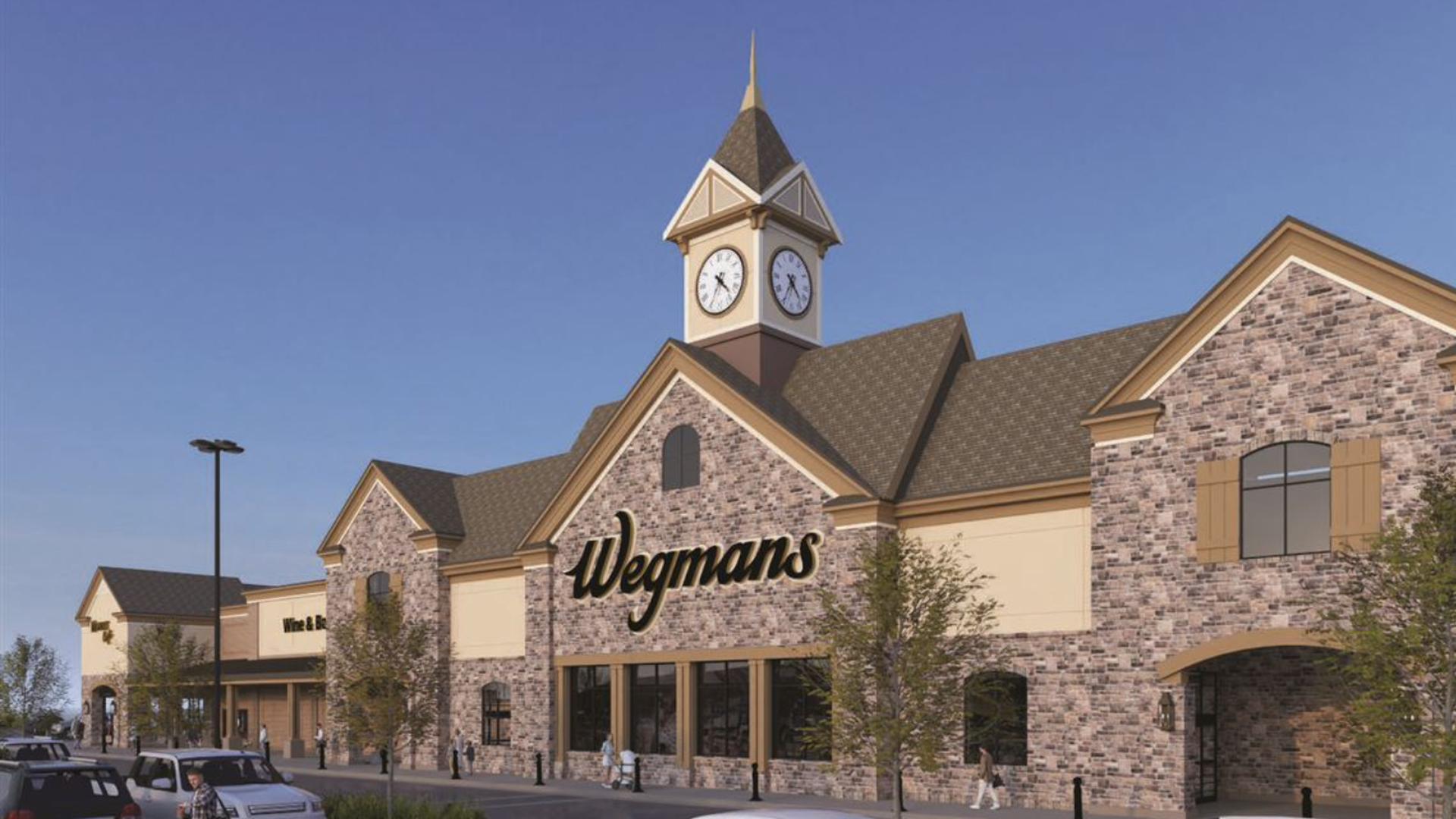 Exterior of a Wegmans store with a clock tower, brick facade, and beige accents under a clear blue sky. Several people walk and cars park in front of the store.