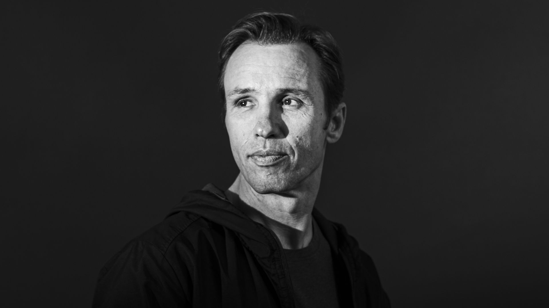 Black and white portrait of author Markus Zusak, white man wearing hoodie and tshirt. 