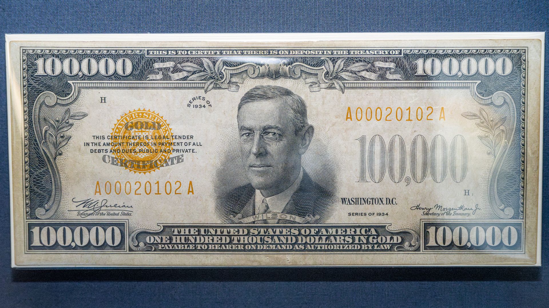 Close-up of a 1934 United States Gold Certificate worth $100,000, with a portrait of Woodrow Wilson in the center, ornate blue border, large "100,000" numerals in the corners, and a gold seal.