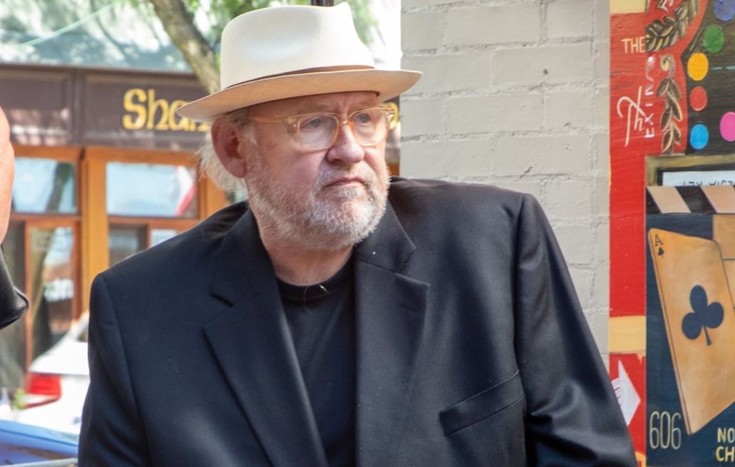 Tony Fitzpatrick wearing a white hat, yellow glasses and a black blazer. 