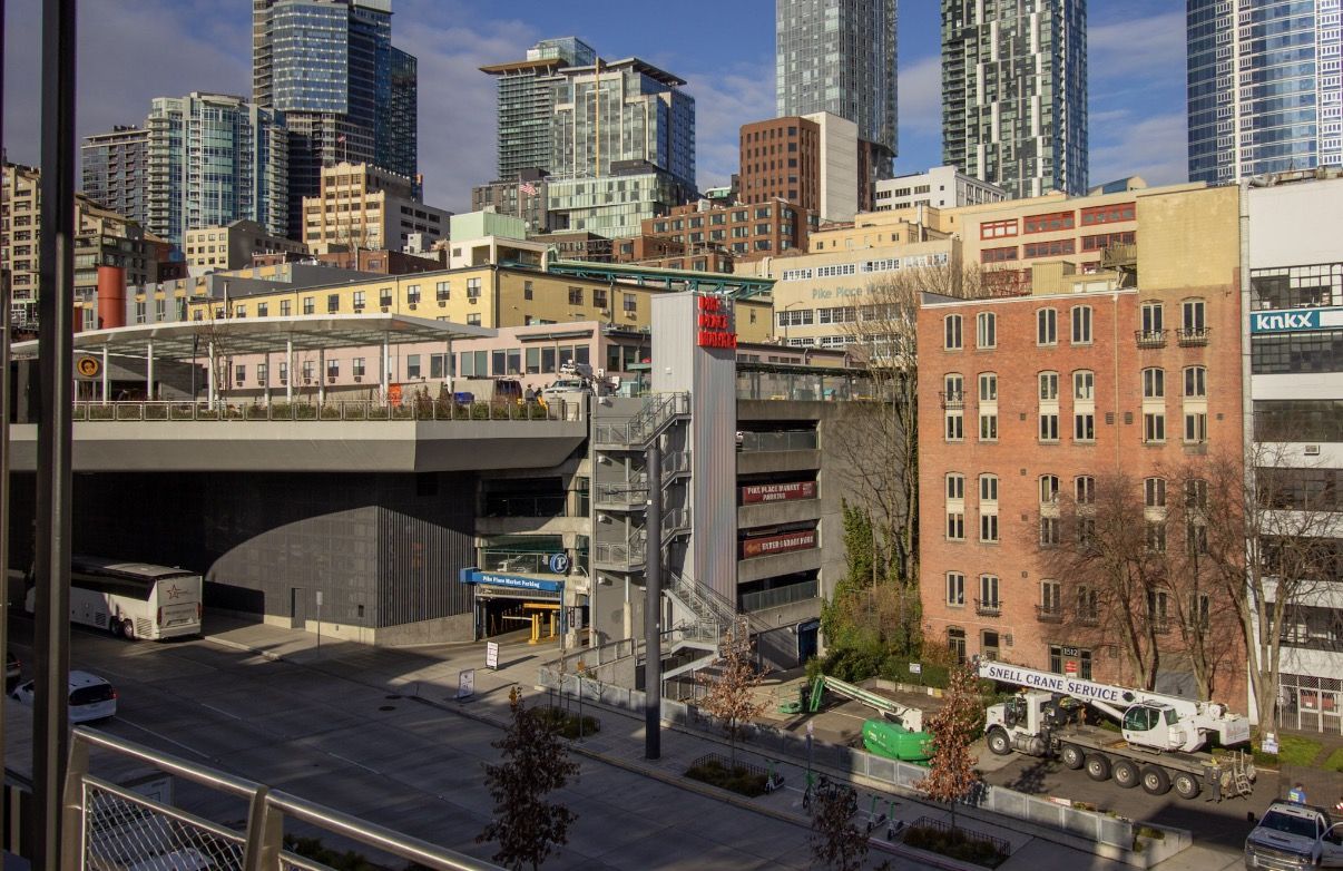 A view of Downtown Seattle and Pike Place market from across Alaskan Way, with a parking garage with a neon red sign that says "Pike Place Market"