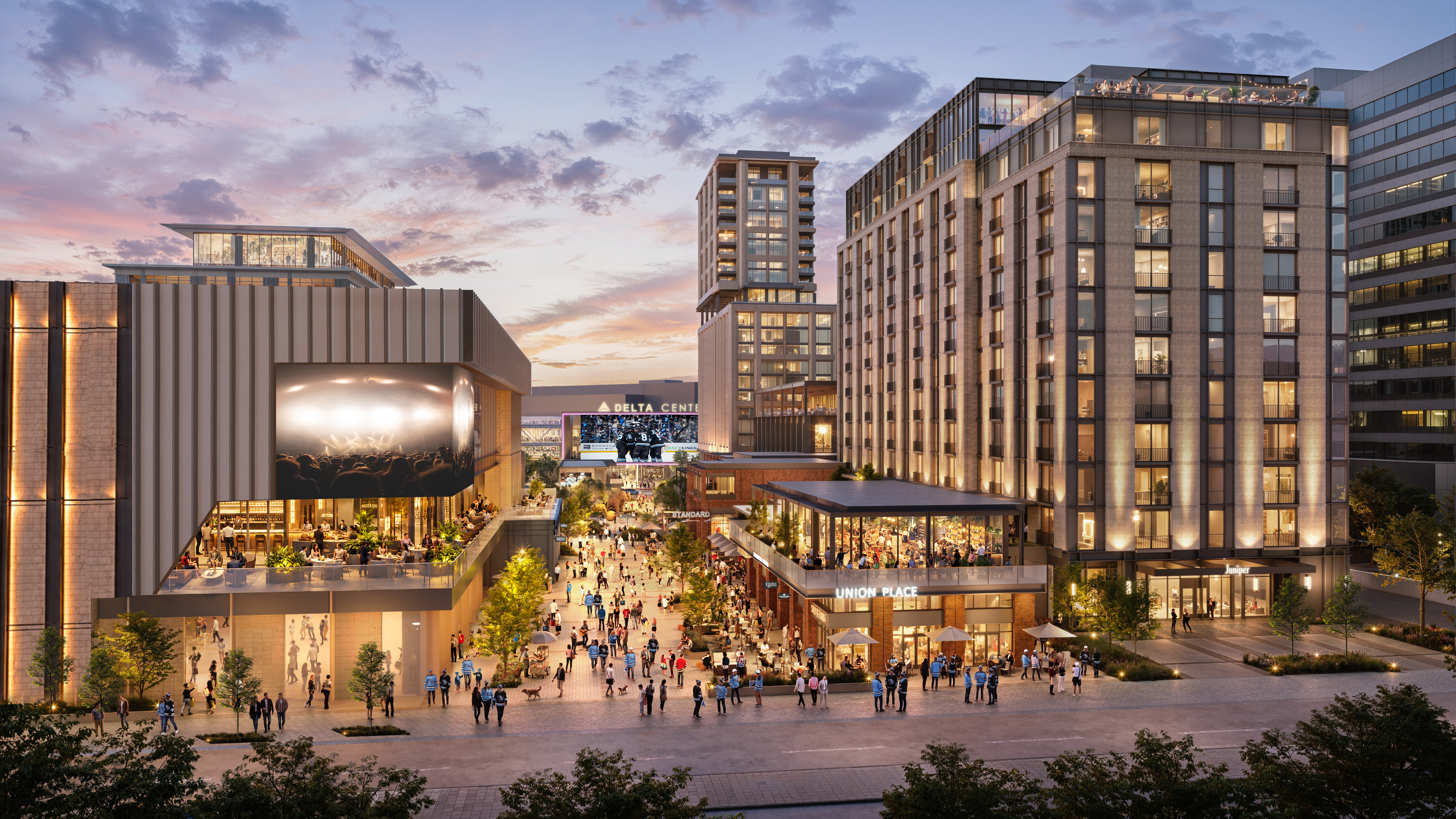 Modern brick-and-glass buildings enclose a bustling outdoor plaza at sunset. People walk, dine on terraces, and a large screen faces the crowd.