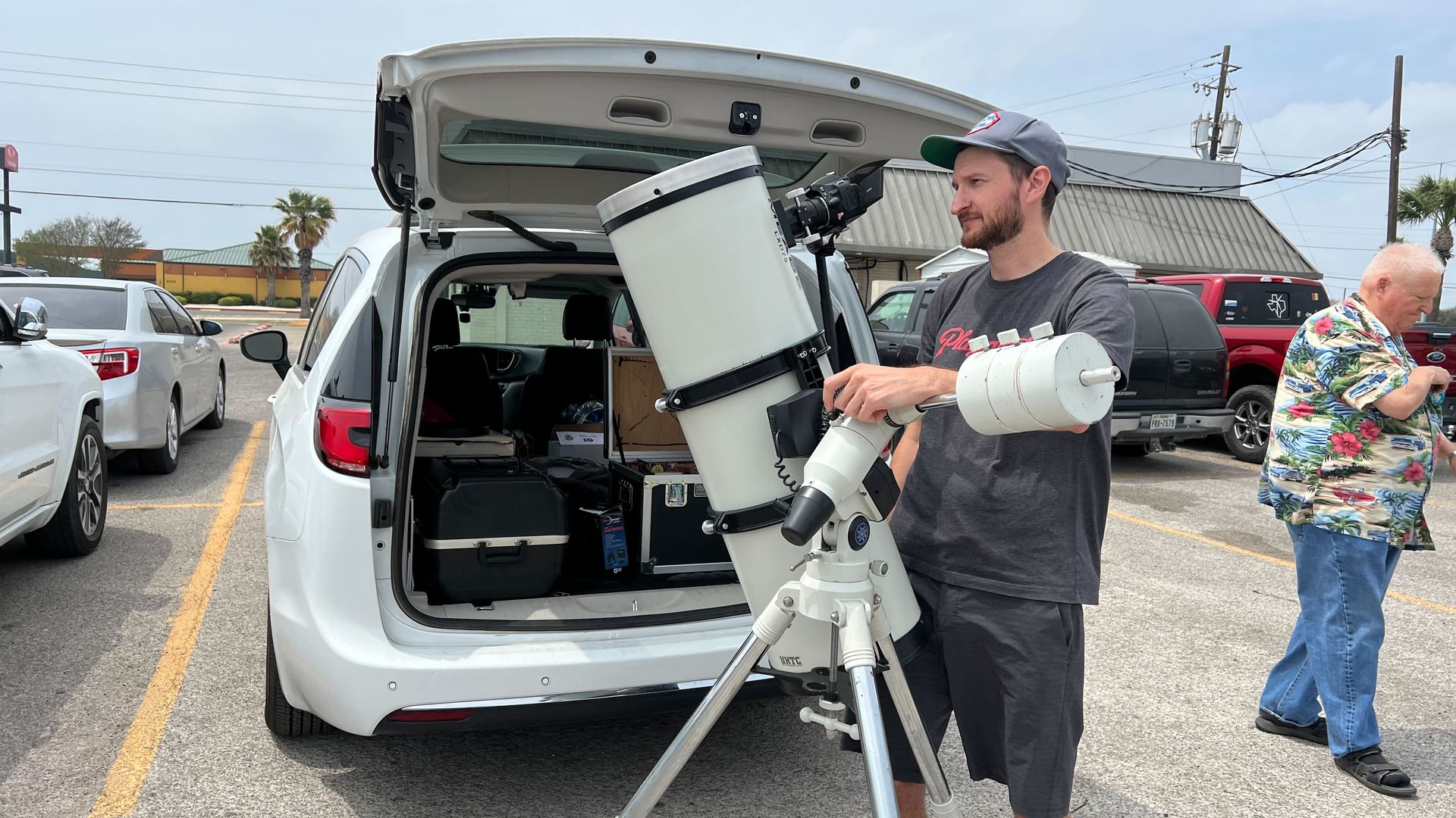 A man standing in a parking lot with a large white telescope