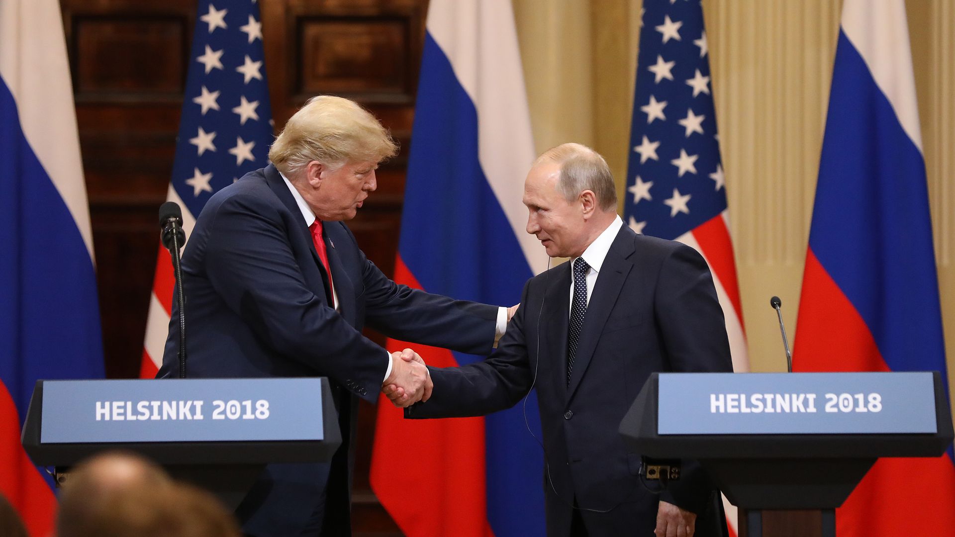 Trump shakes hands with Vladimir Putin behind podiums that say "Helsinki 2018."