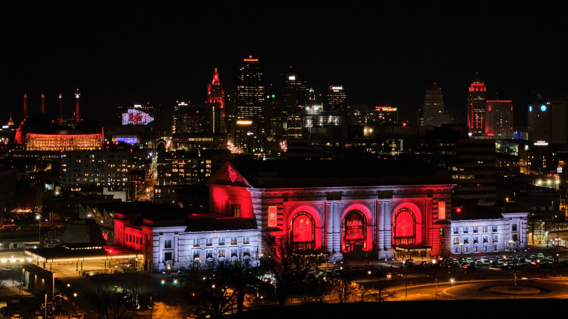 The Kansas City skyline featuring Union Station in the foreground all lit up red and white with a Chiefs logo in lights on the downtown Marriott building at night.