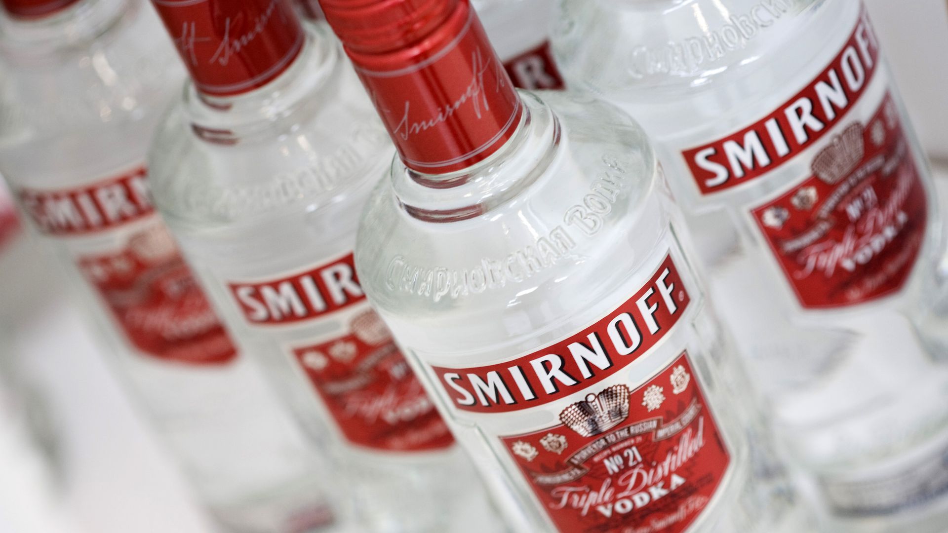Close-up of several Smirnoff vodka bottles with red labels showing the white 'SMIRNOFF' logo, tilted diagonally, clear glass.