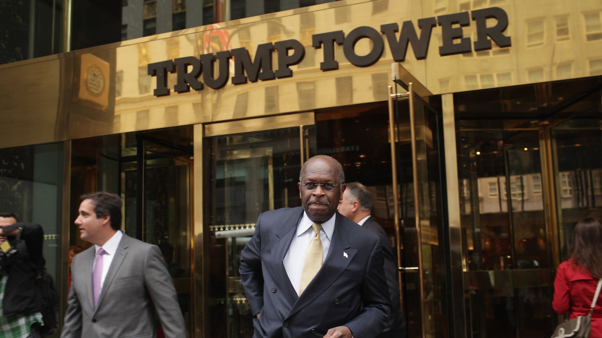 In this image, Herman Cain walks out of Trump Tower in a suit. 