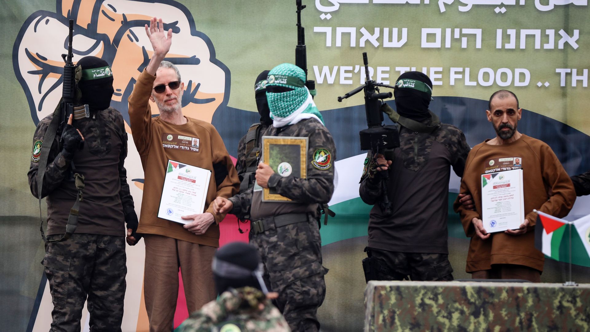 Two hostages in brown released, one waving, both held by armed, masked soldiers