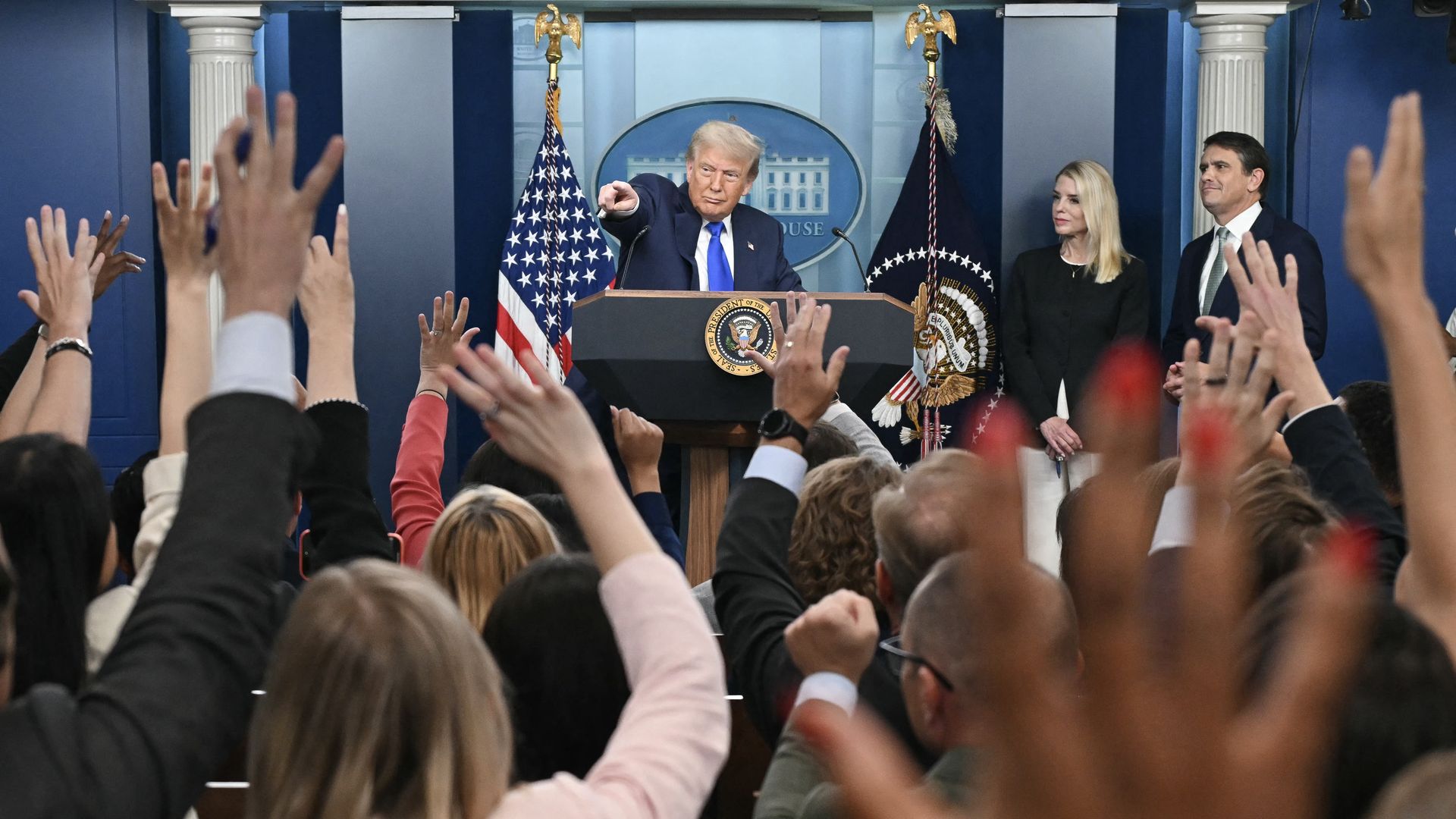 A group of reporters sits with hands raised as Trump points to one of them 