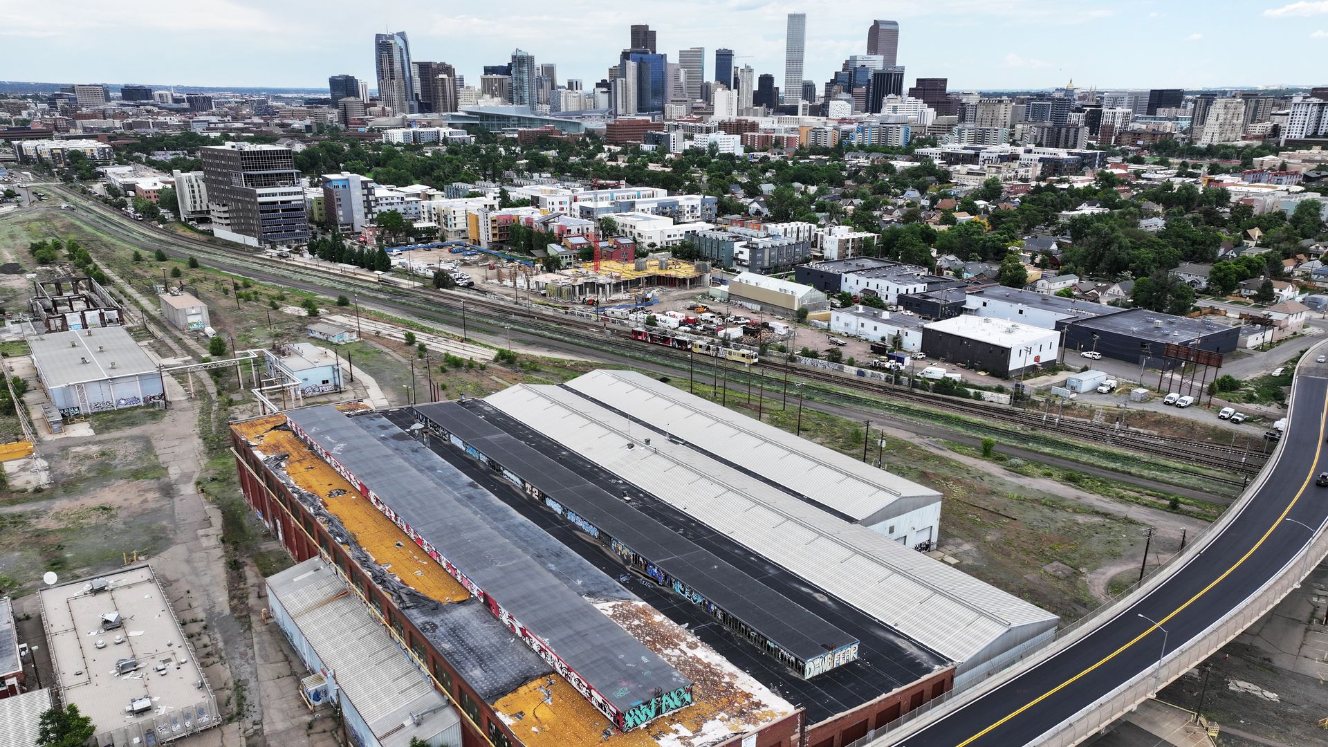An industrial area next to a roadway, with the skyline of Denver in the background. 