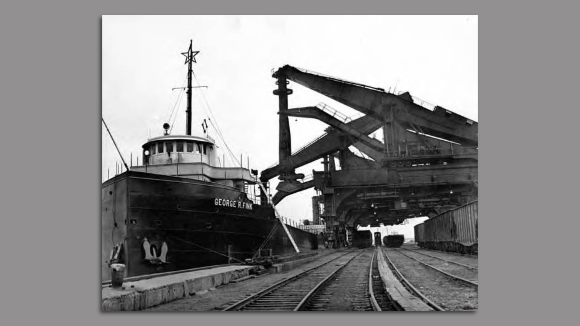 Historical black and white photo of "Hulett Unloaders" unloading Great Lakes steam ship of iron ore. 