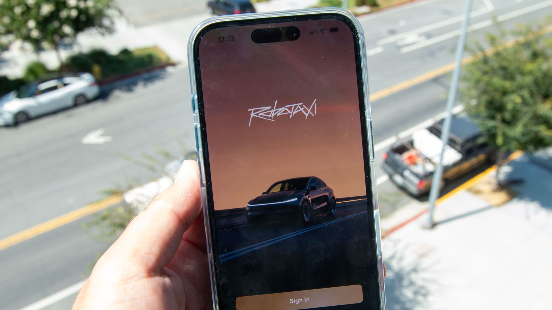 Hand holding a smartphone displaying a ride-hailing app; screen shows a car image and a "Sign In" button, with a blurred city street in the background.