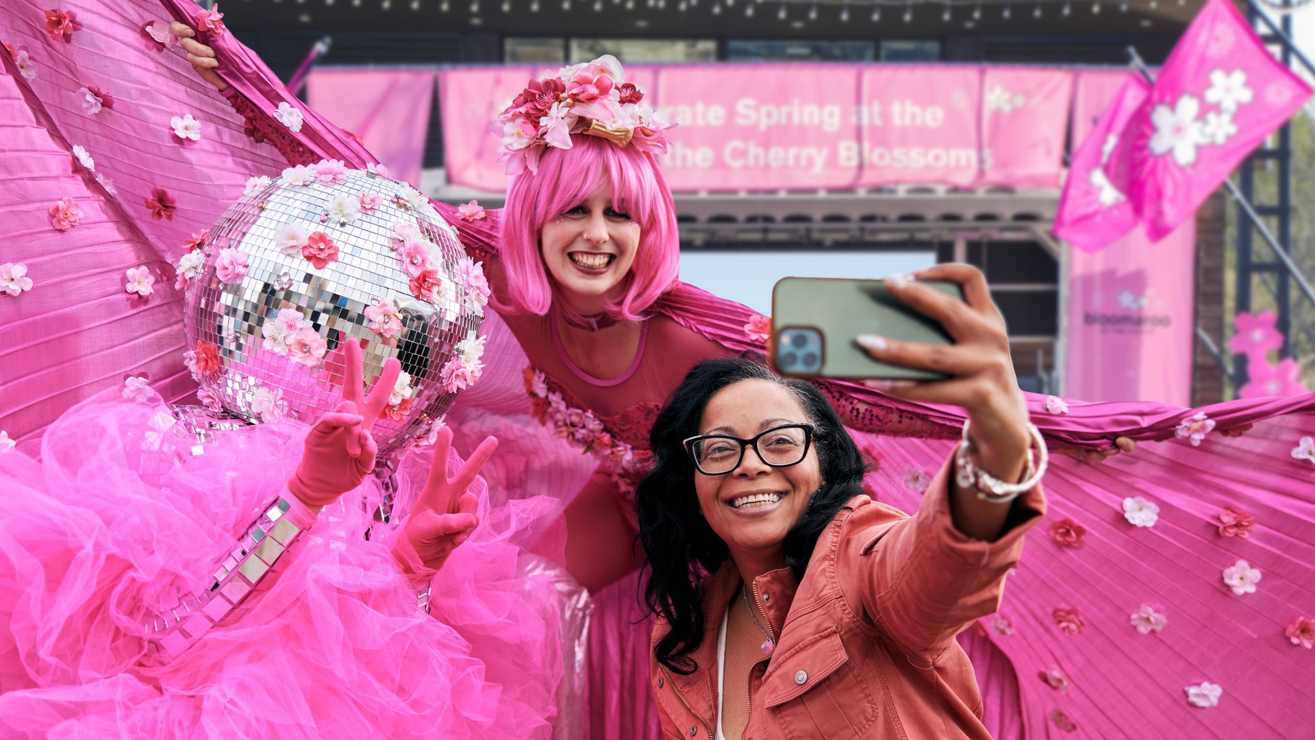 Two people in cherry blossom festival outfits take a selfie with a visitor