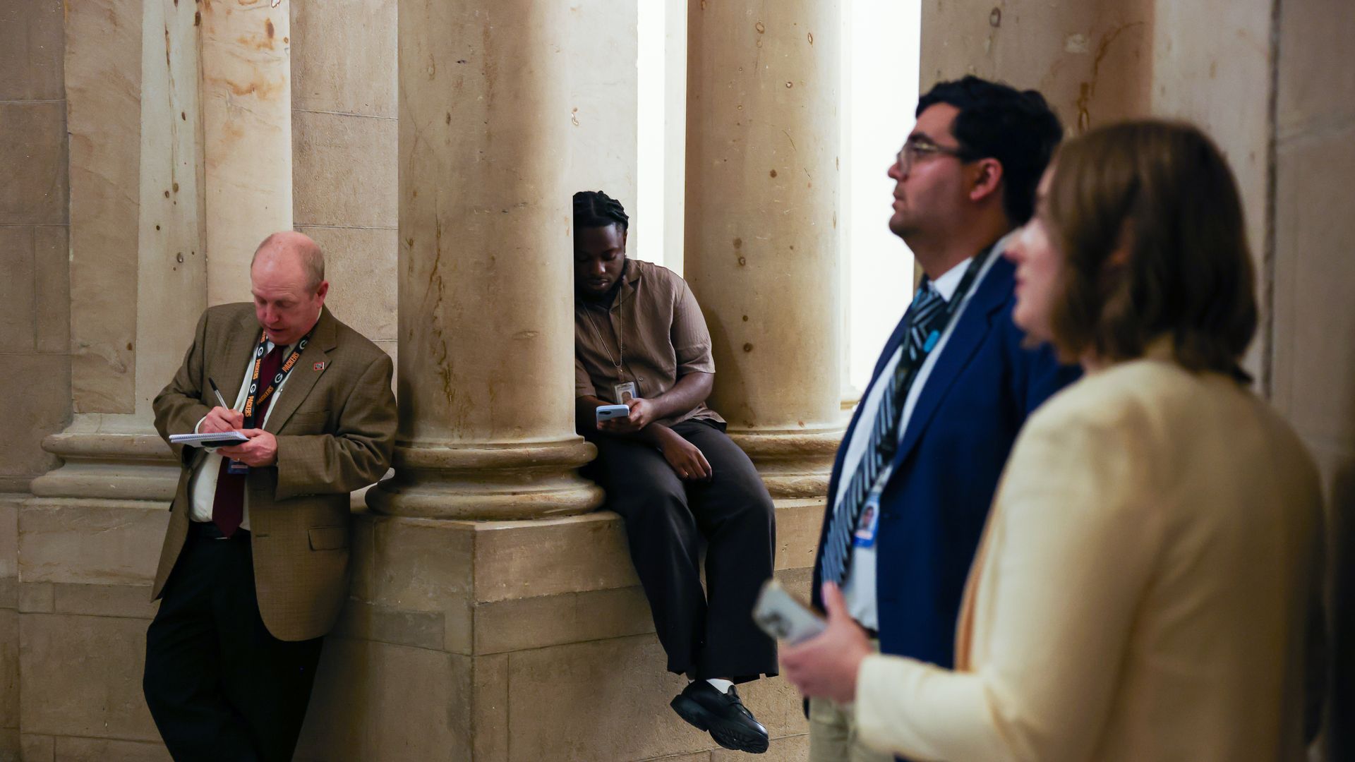 People trying to get comfortable in the middle of a very official looking building as they wait. 