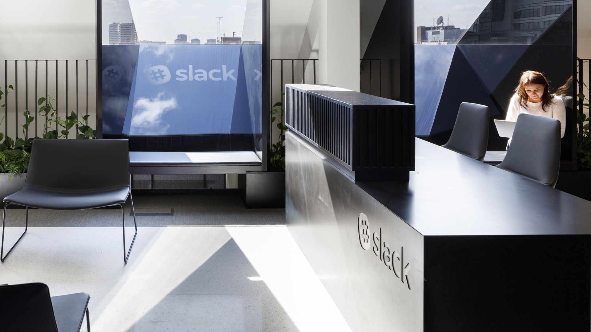 Office lobby of Slack. With woman sitting at a desk and a TV on.