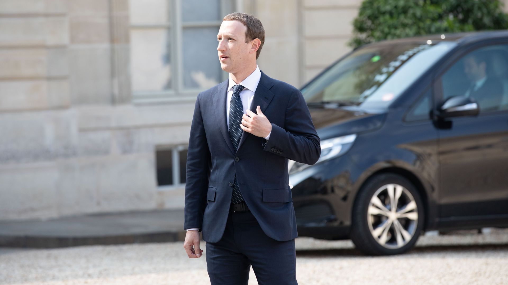 Mark Zuckerberg stands outside in a suit
