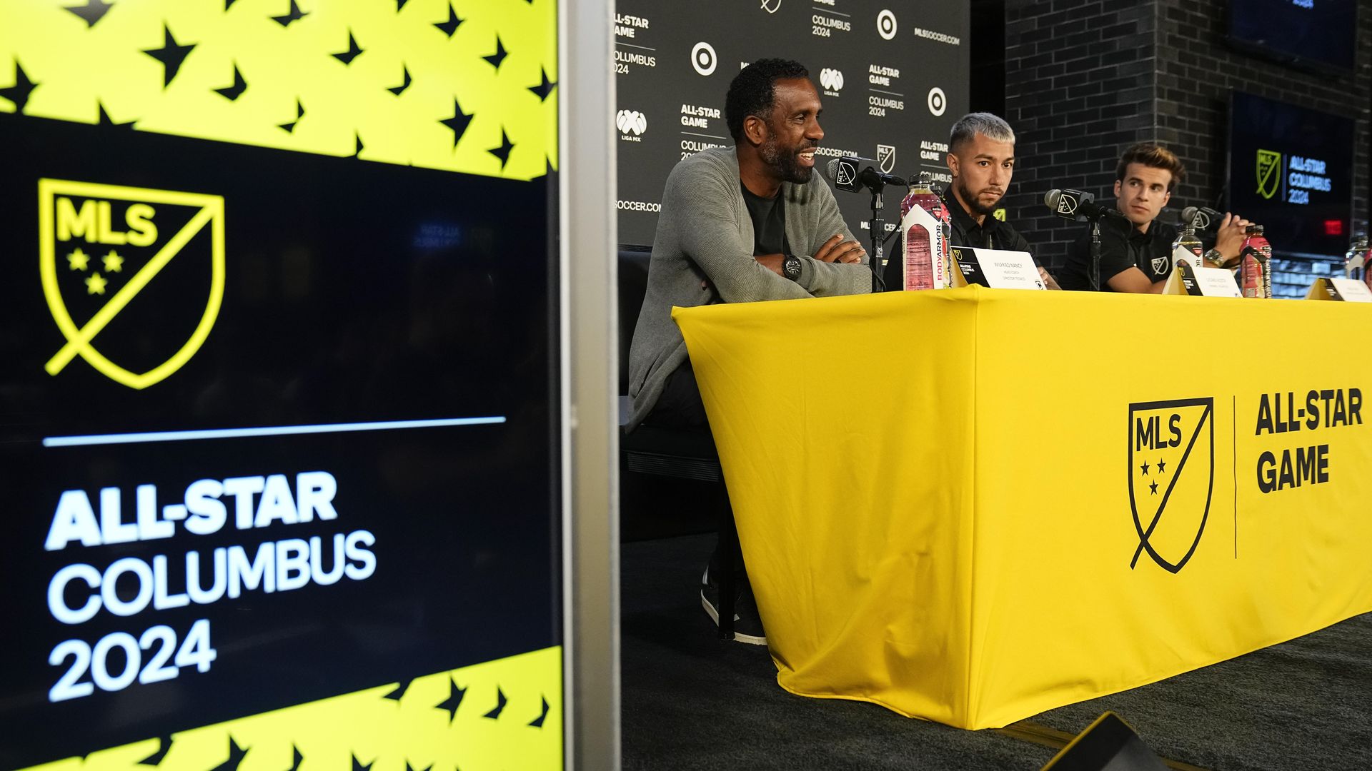 Crew head coach Wilfried Nancy, who will be coaching the MLS All-Stars, sits at a news conference in the background, with an "All-Star Columbus 2024" sign in the foreground