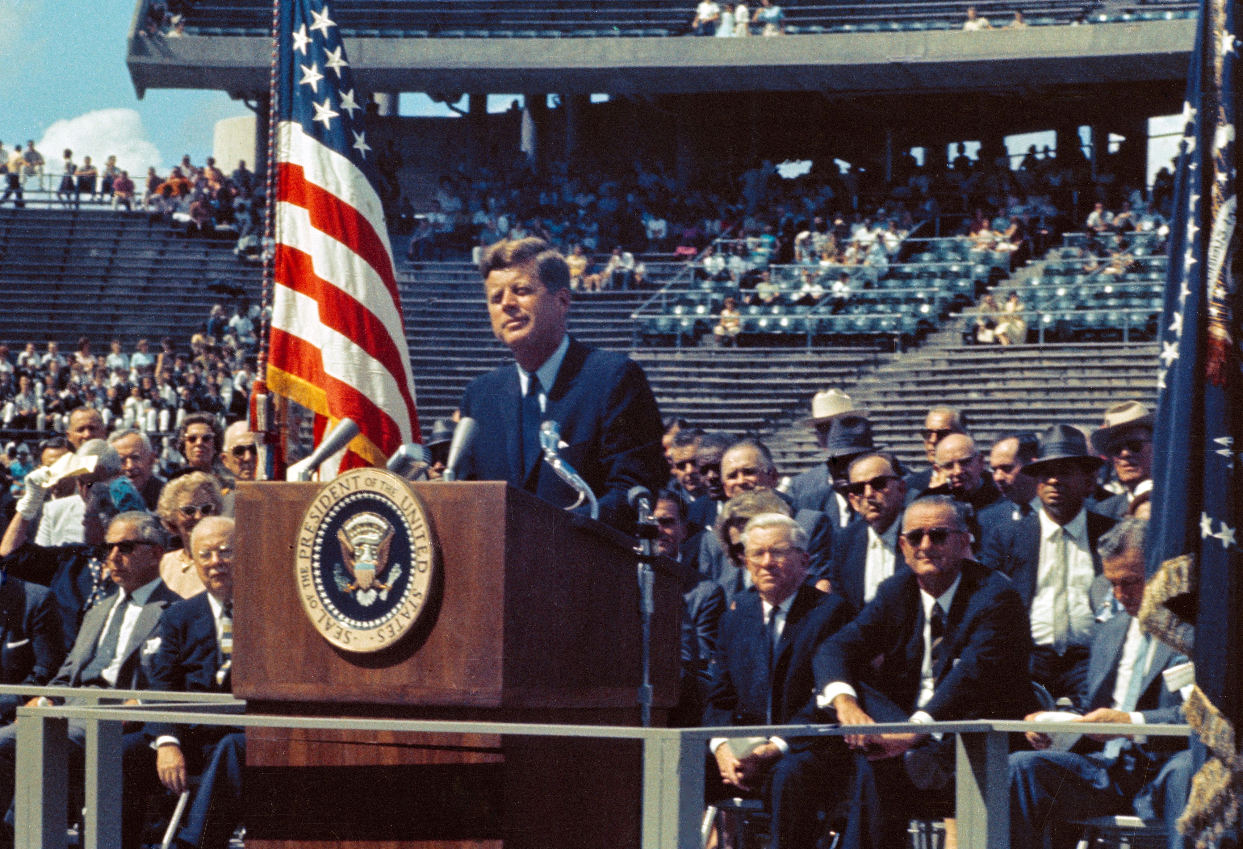 Photo of JFK in front of podium in a stadium. 
