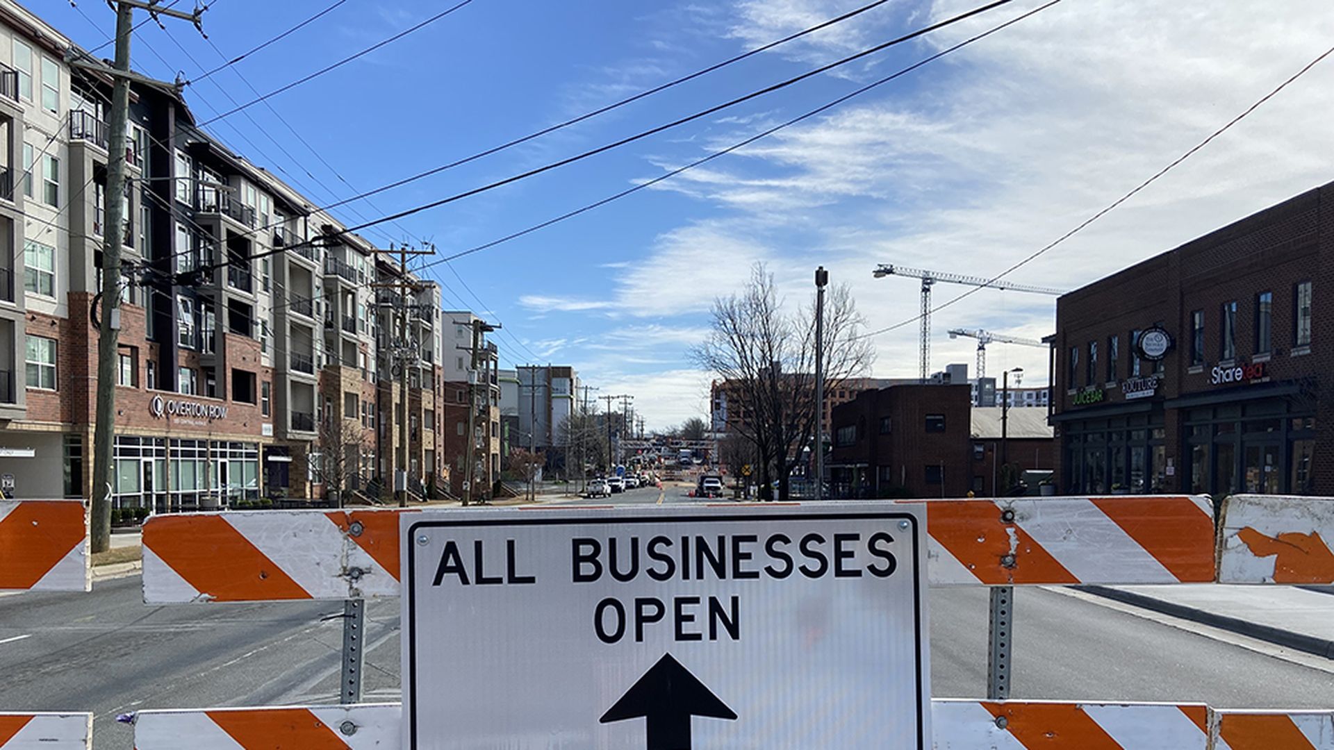 A sign reading "All businesses open" with an arrow pointing forward and "No thru traffic" blocks off Central Avenue on a sunny day.