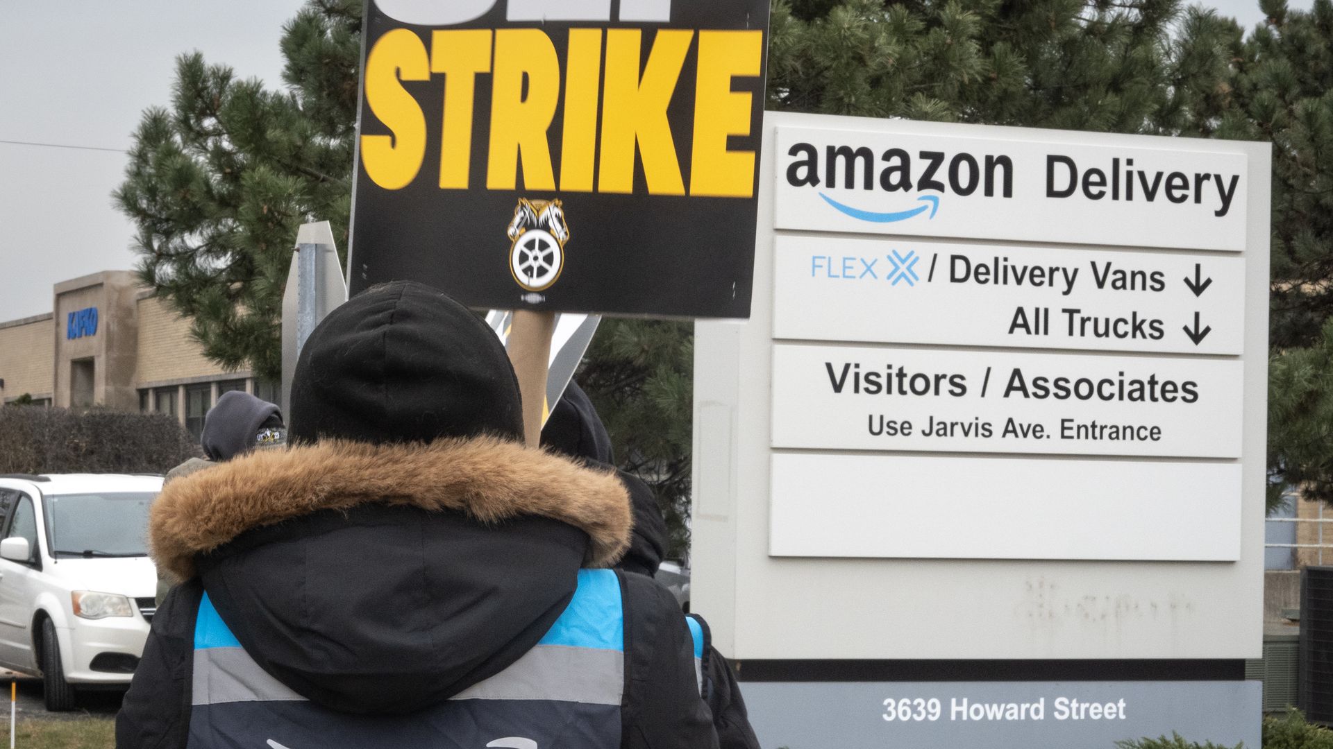 A worker holds up a strike sign in front of an Amazon Delivery warehouse sign.