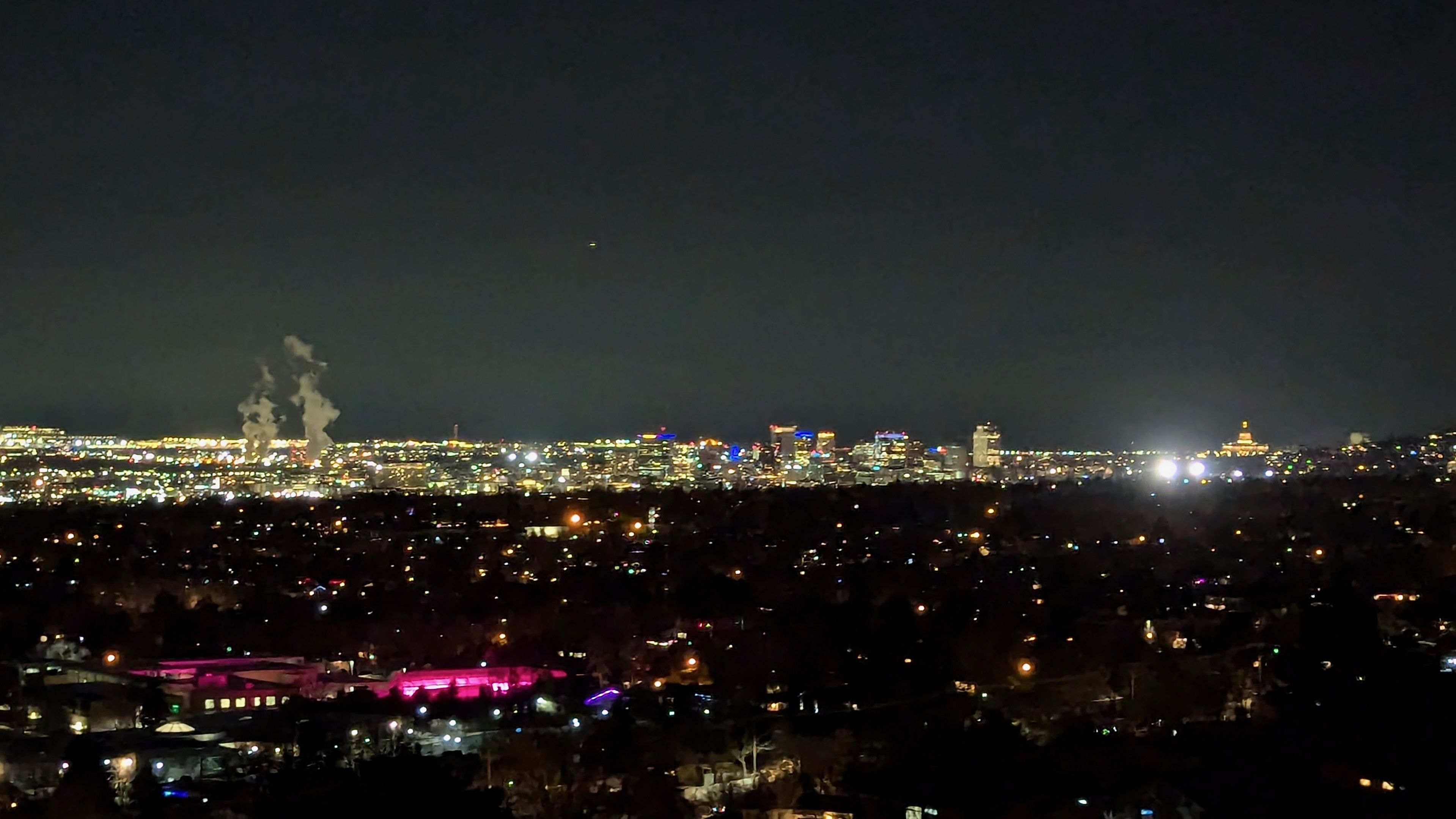 A city at night, viewed from a hill nearby.
